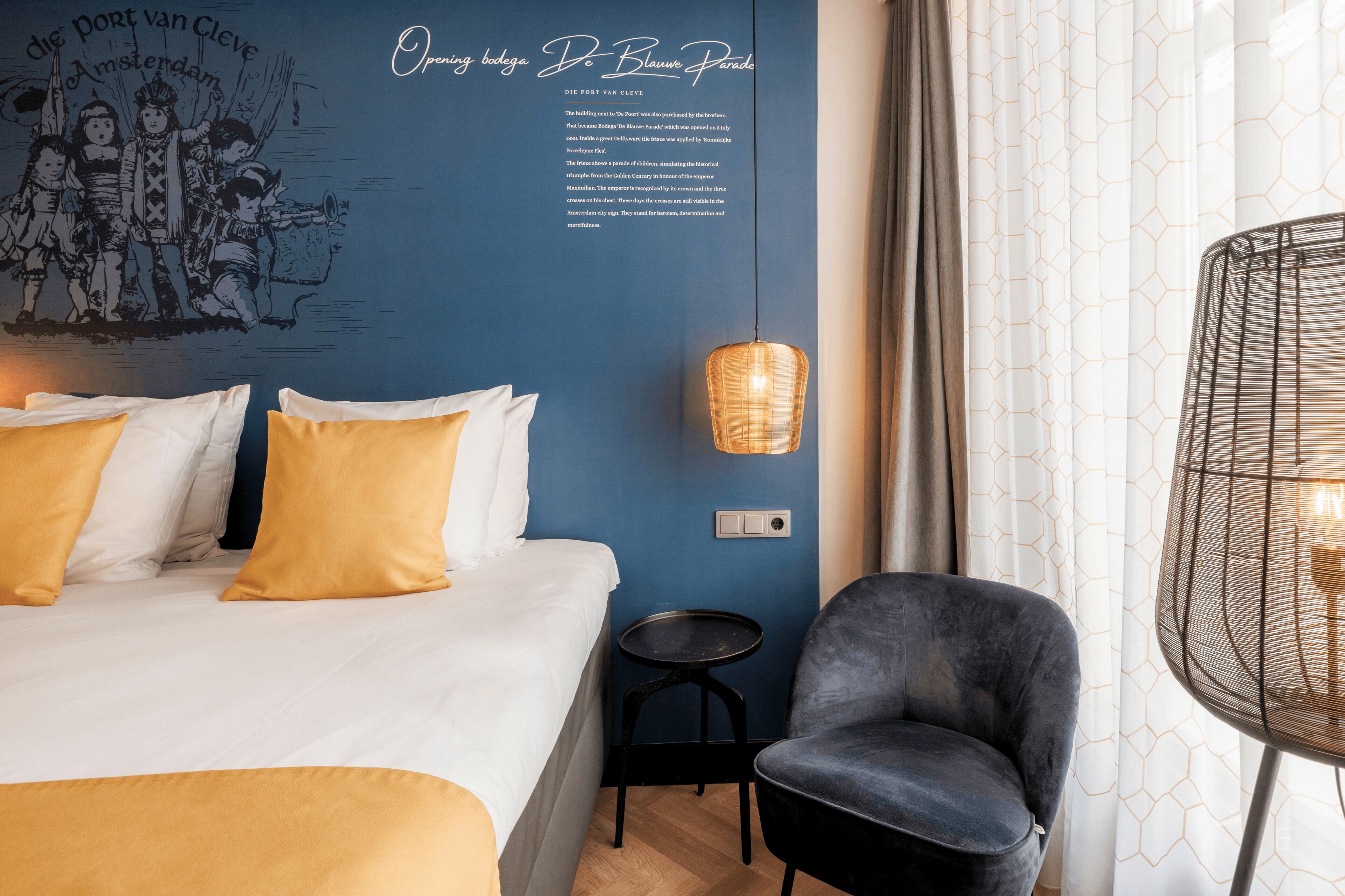 A hotel room with a bed, a chair, a small table, and a wall with a mural and text.