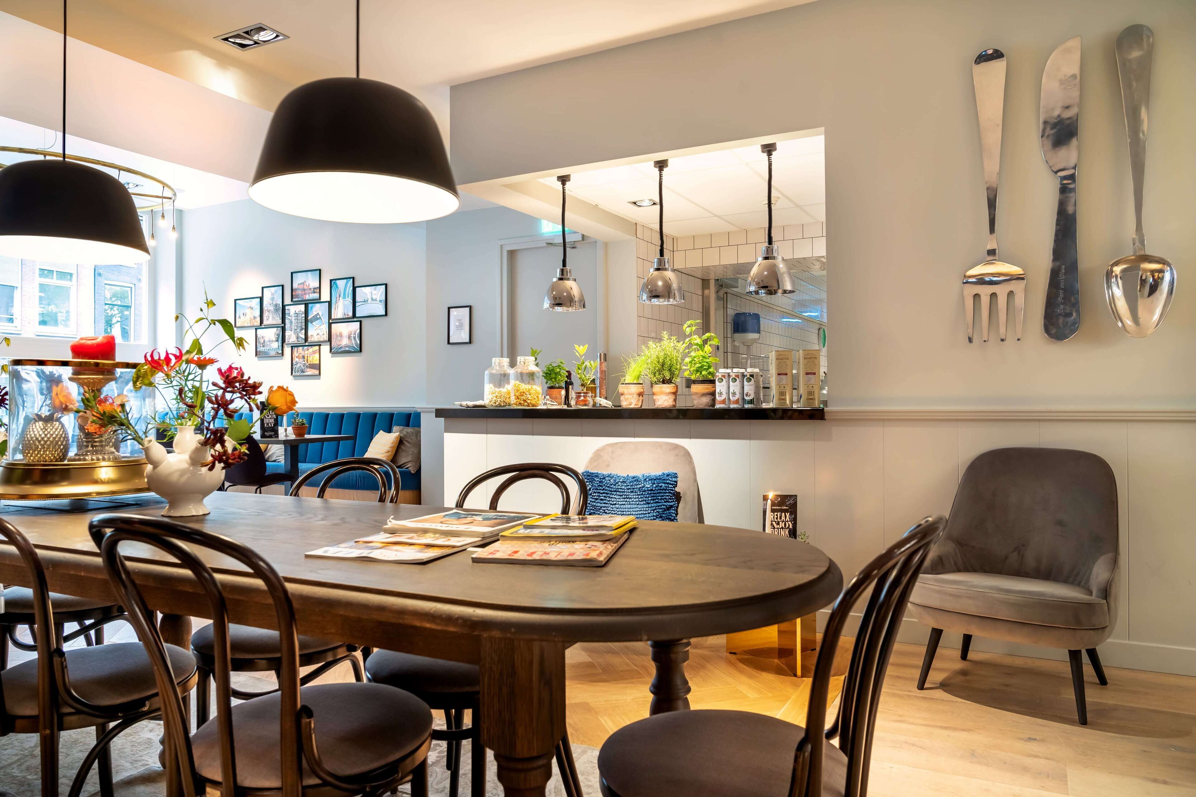 A dining area with a wooden table, chairs, pendant lights, and a kitchen in the background.