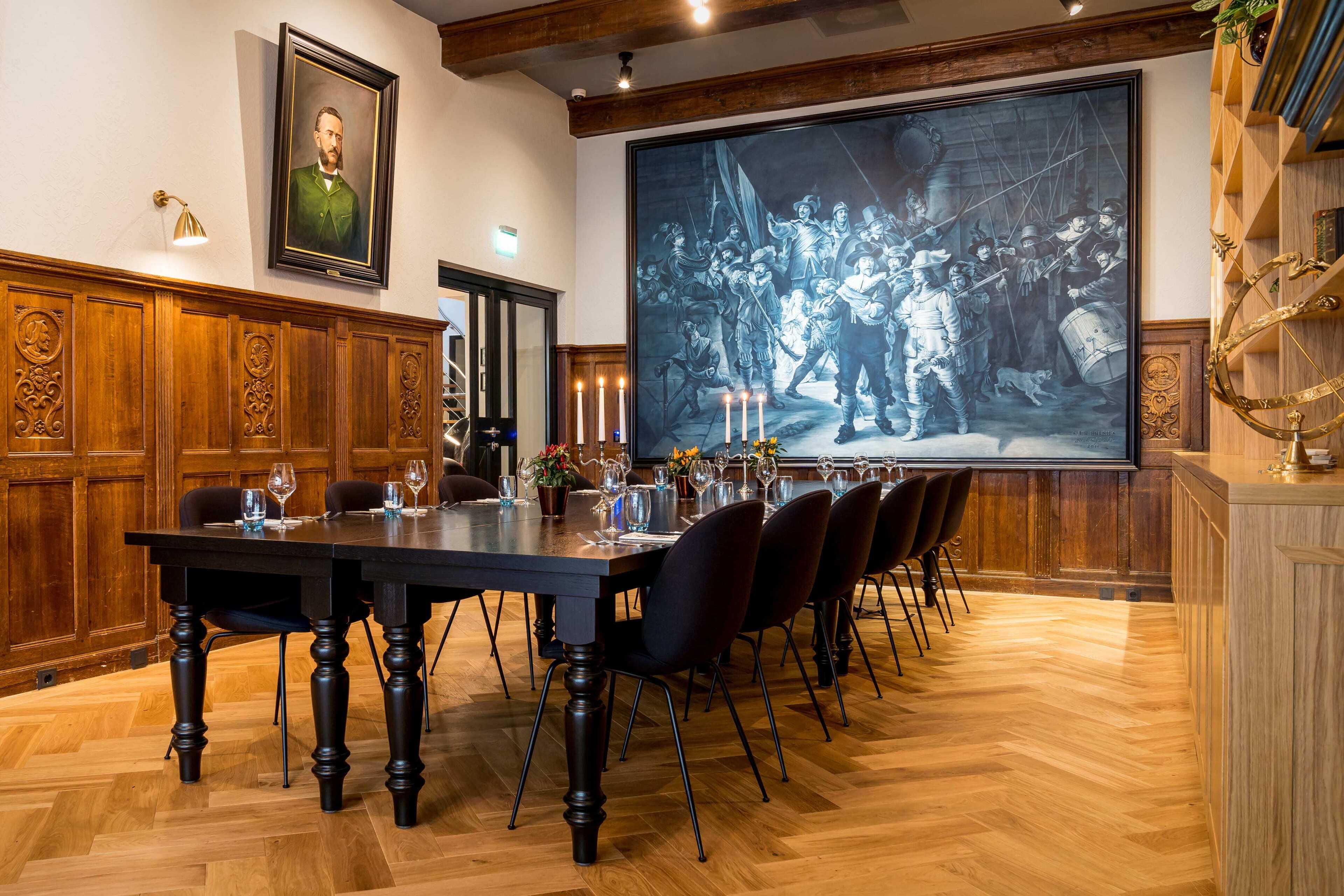 A dining area with a long table, chairs, candles, and a large framed picture on the wall.
