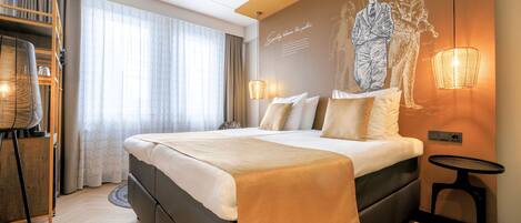 Una habitación de hotel moderna con una cama grande, un escritorio con silla, una lámpara de pie y un aplique de pared.