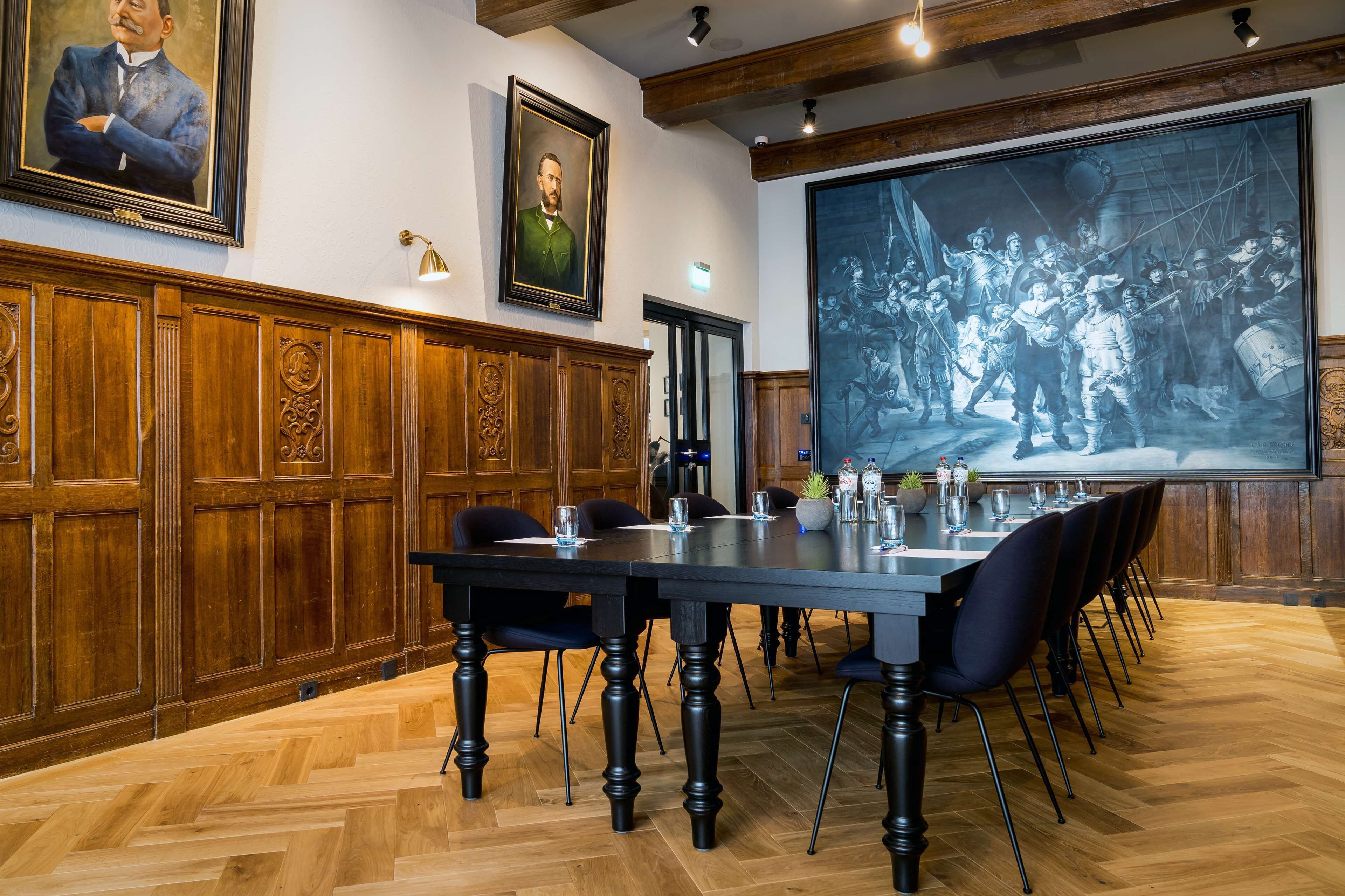 A conference room with a large table, wooden paneling, and framed portraits on the walls.