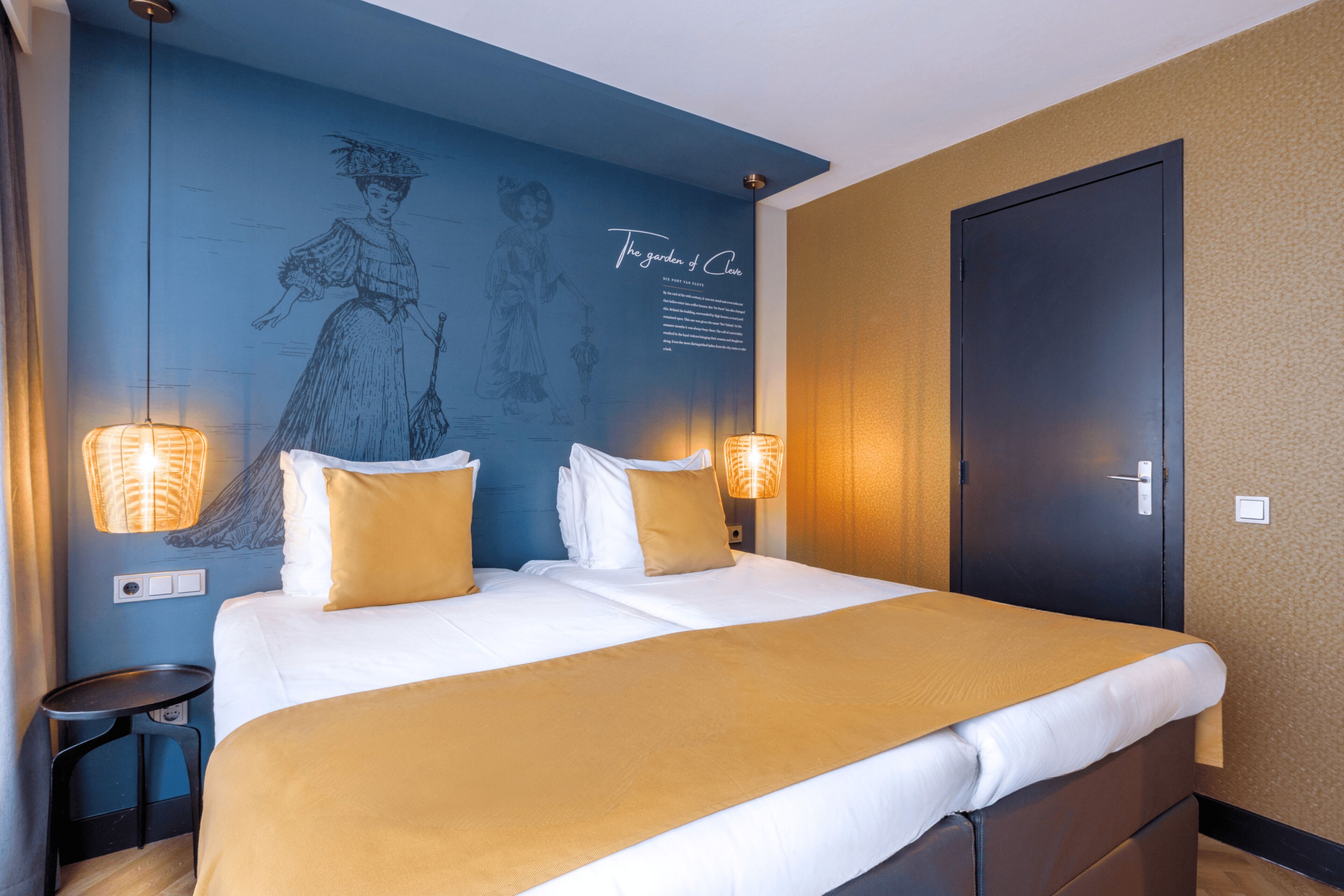 Una habitació d'hotel amb un llit gran, dues làmpades de nit, una porta fosca i un mural a la paret.