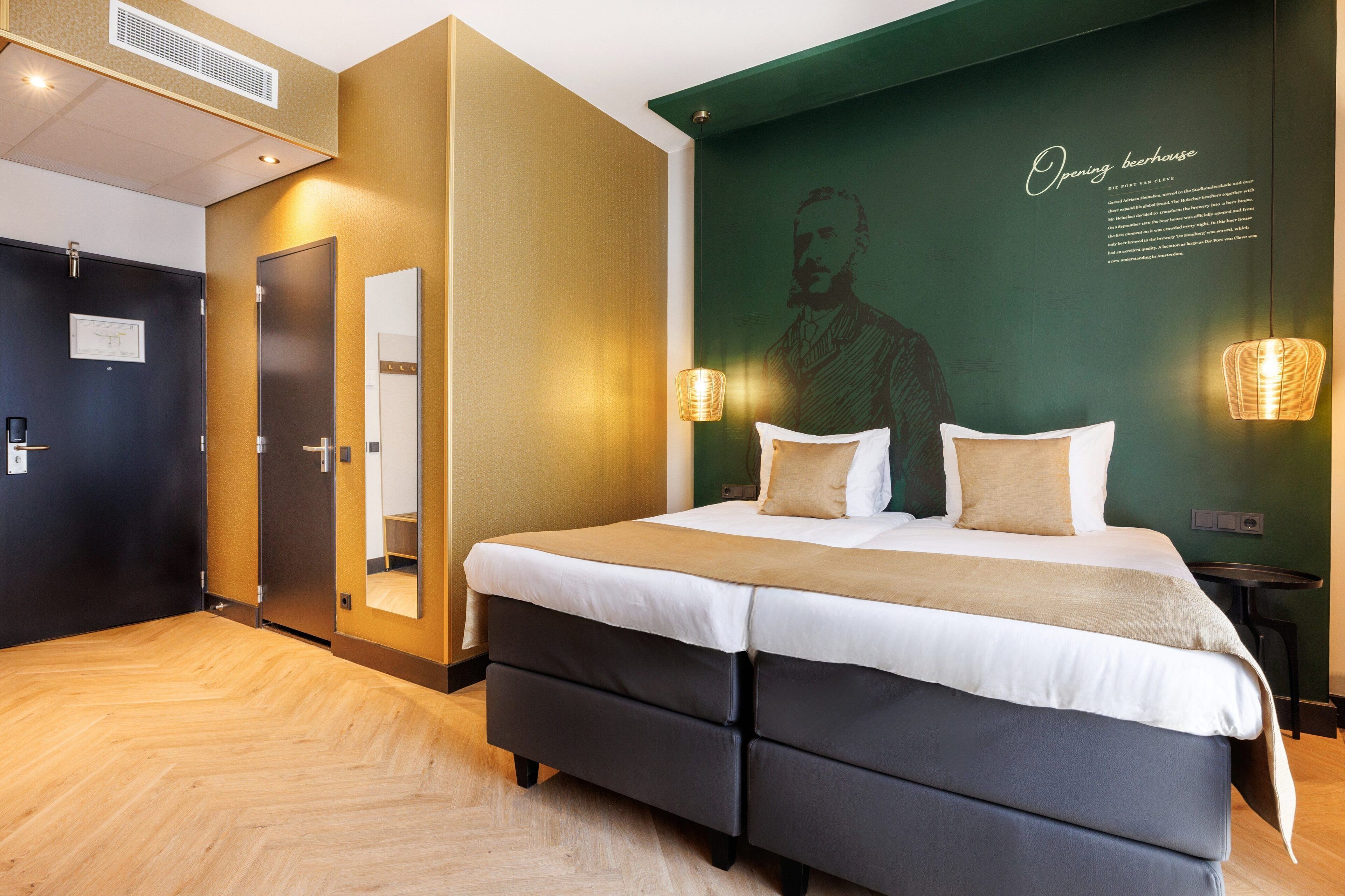 A modern hotel room with a large bed, a mirror, and a wall with a portrait and text.