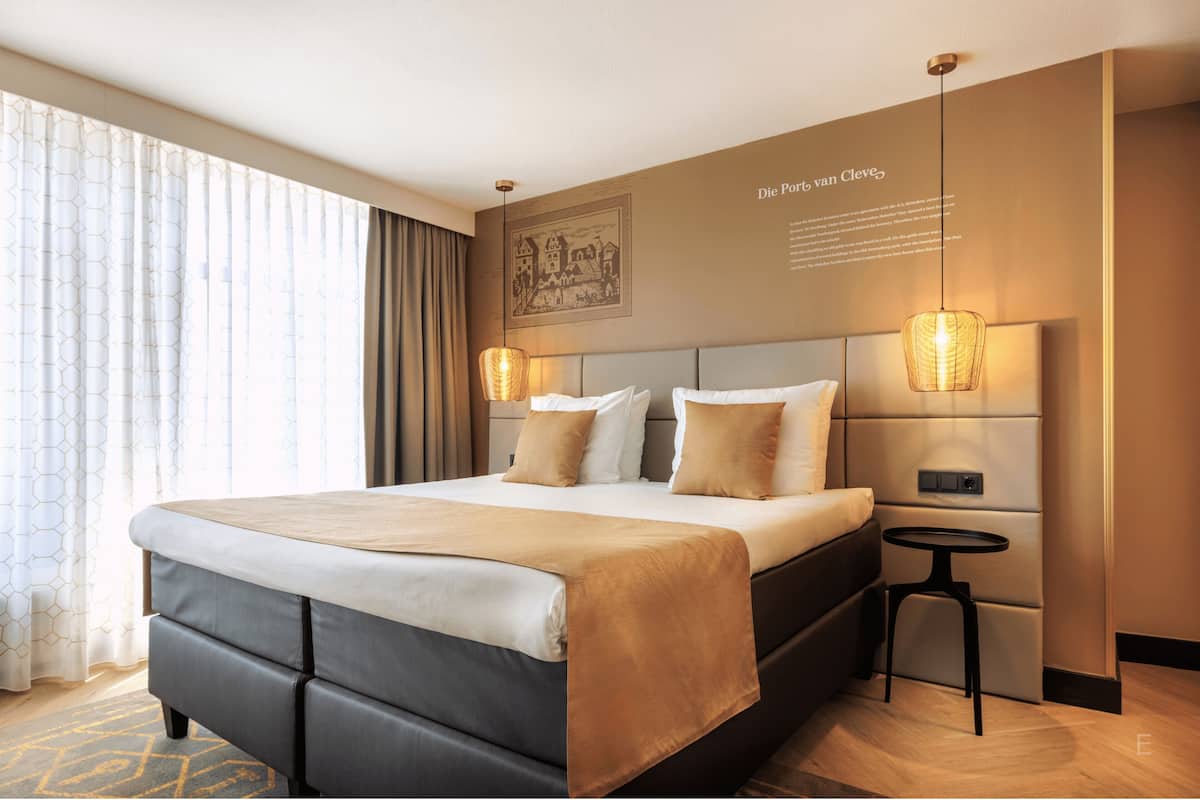 A hotel room with a large bed, two bedside tables, a wall-mounted lamp, and a framed picture.
