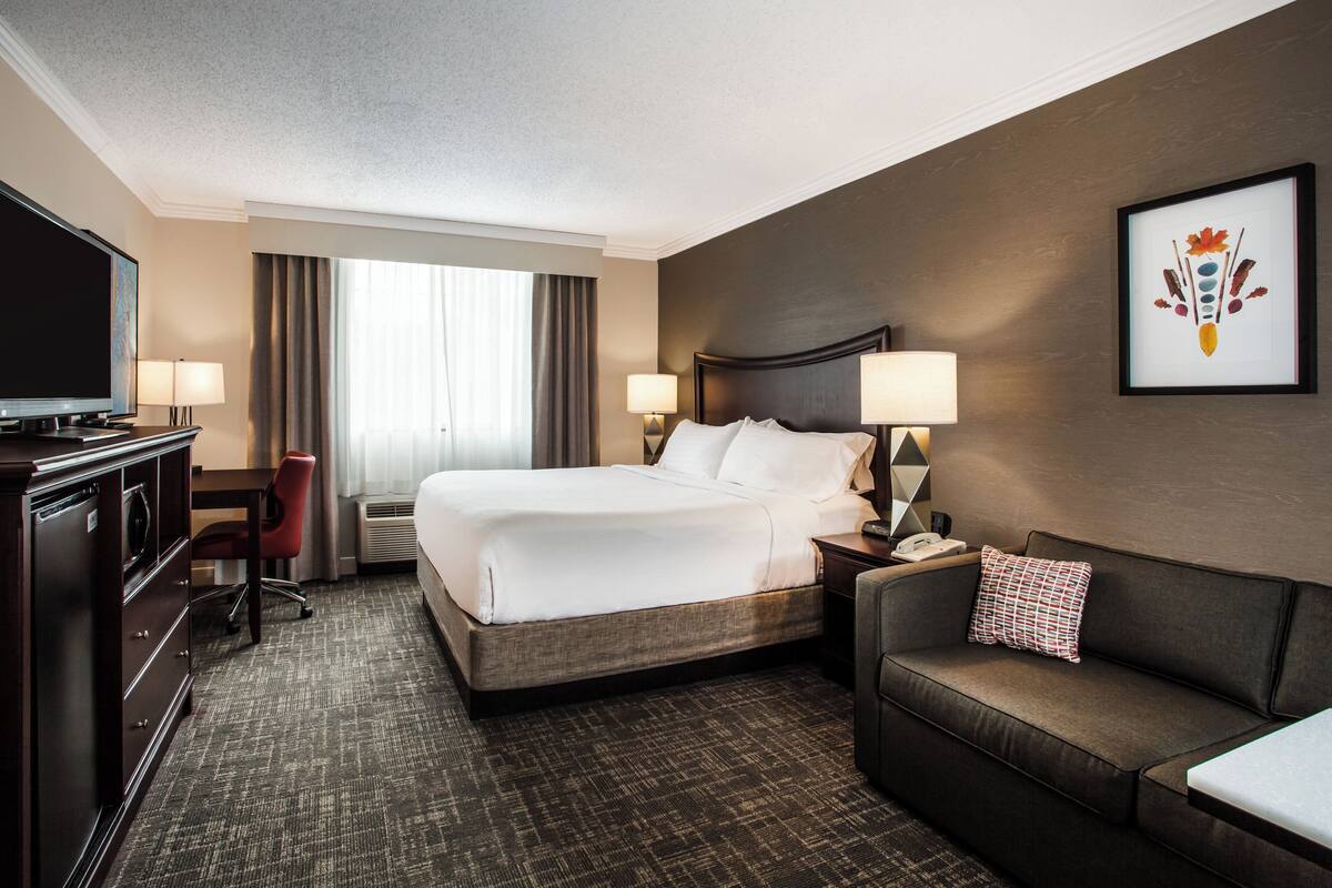 A hotel room with a large bed, a desk with a TV, a sofa, and a framed picture on the wall.