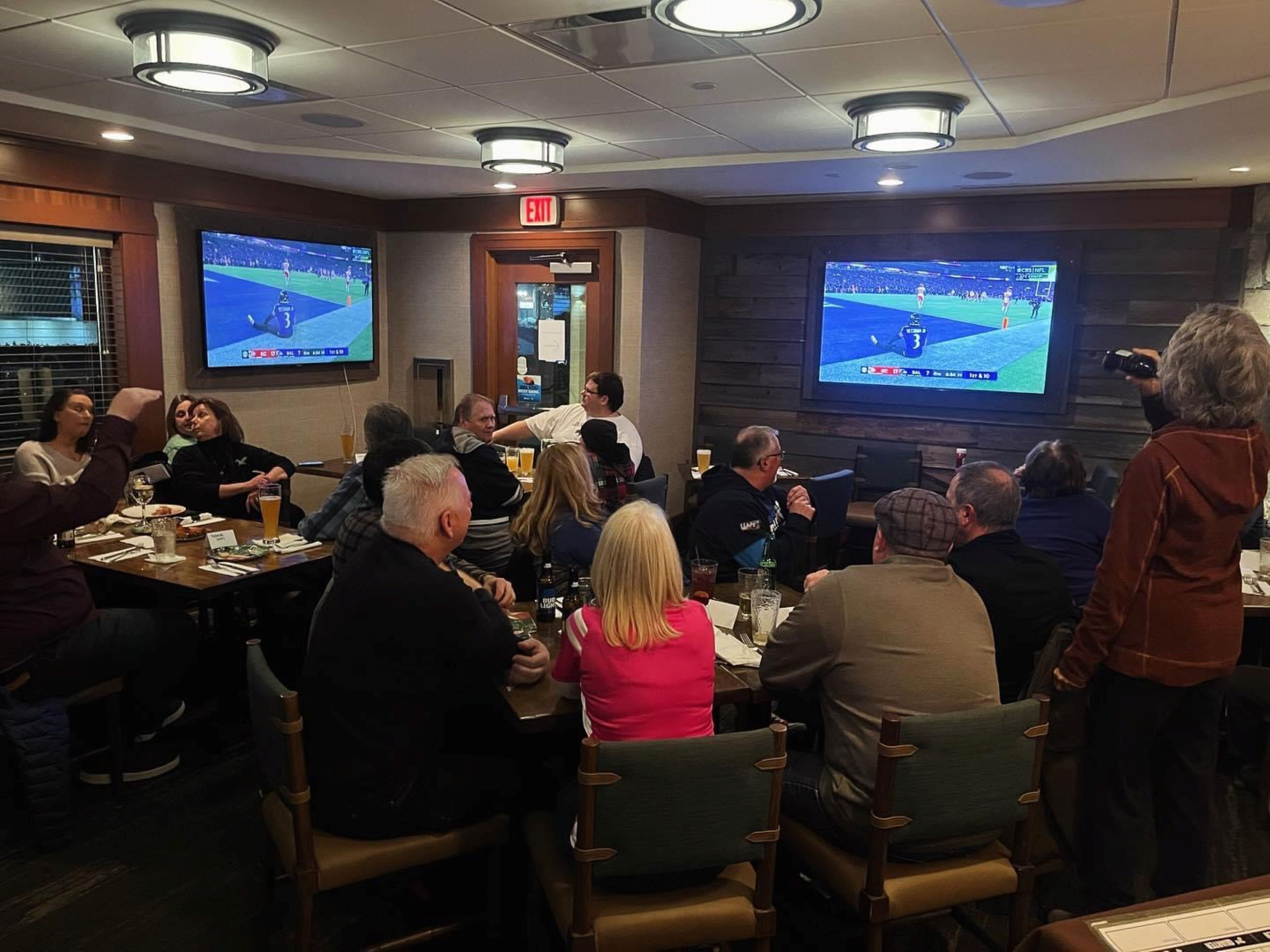 A conference room with multiple screens displaying sports events, tables with drinks, and attendees seated.