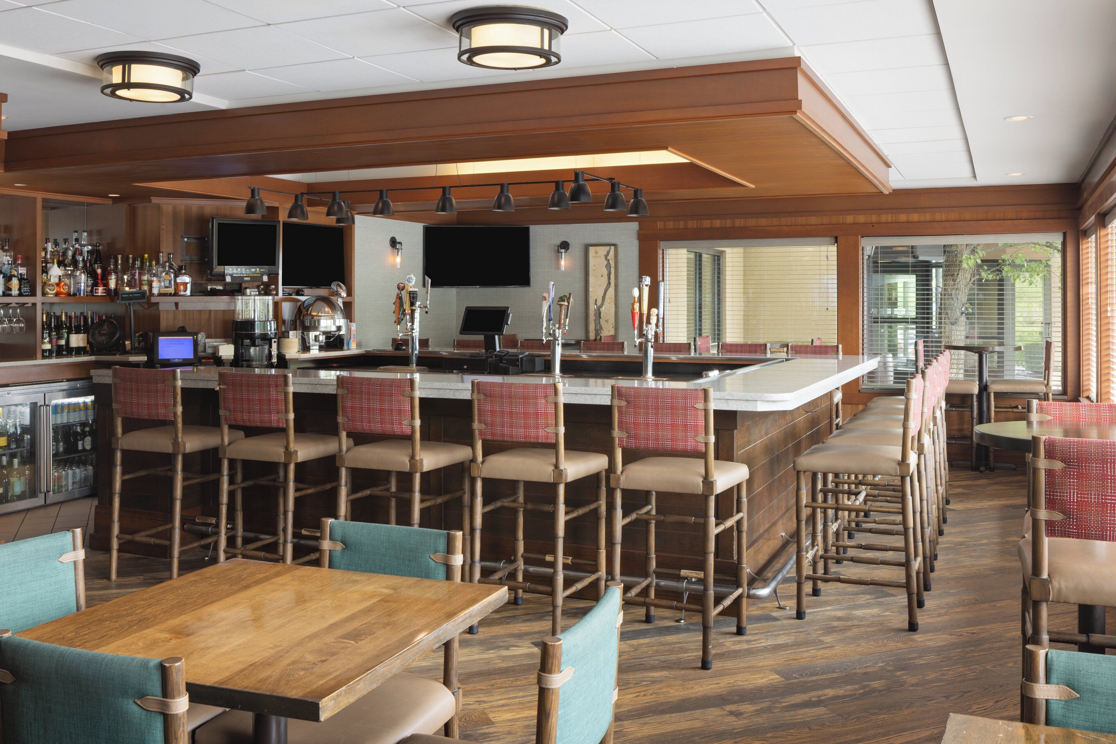 A bar area with multiple seating options, including bar stools and chairs, a television screen, and a variety of bottles and glasses on the bar counter.