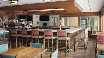 A bar area with multiple seating options, including bar stools and chairs, a television screen, and a variety of bottles and glasses on the bar counter.
