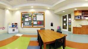 A conference room with a wooden table, chairs, a bulletin board, a kitchenette, and a colorful floor. - Holiday Inn Resort Lake George - Adirondack Area by IHG (Lake George)