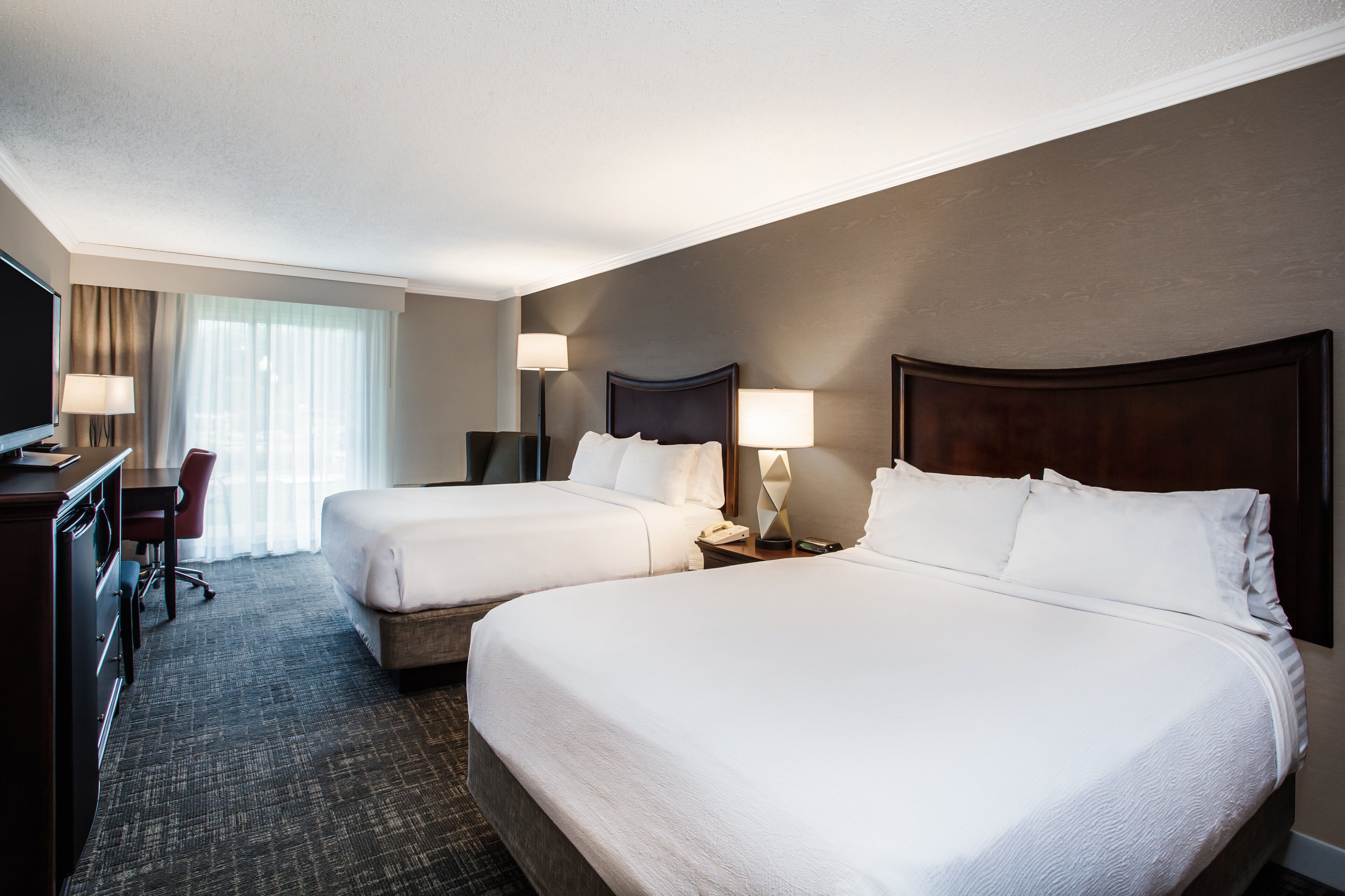 A hotel room with two beds, a desk, a chair, and a television.
