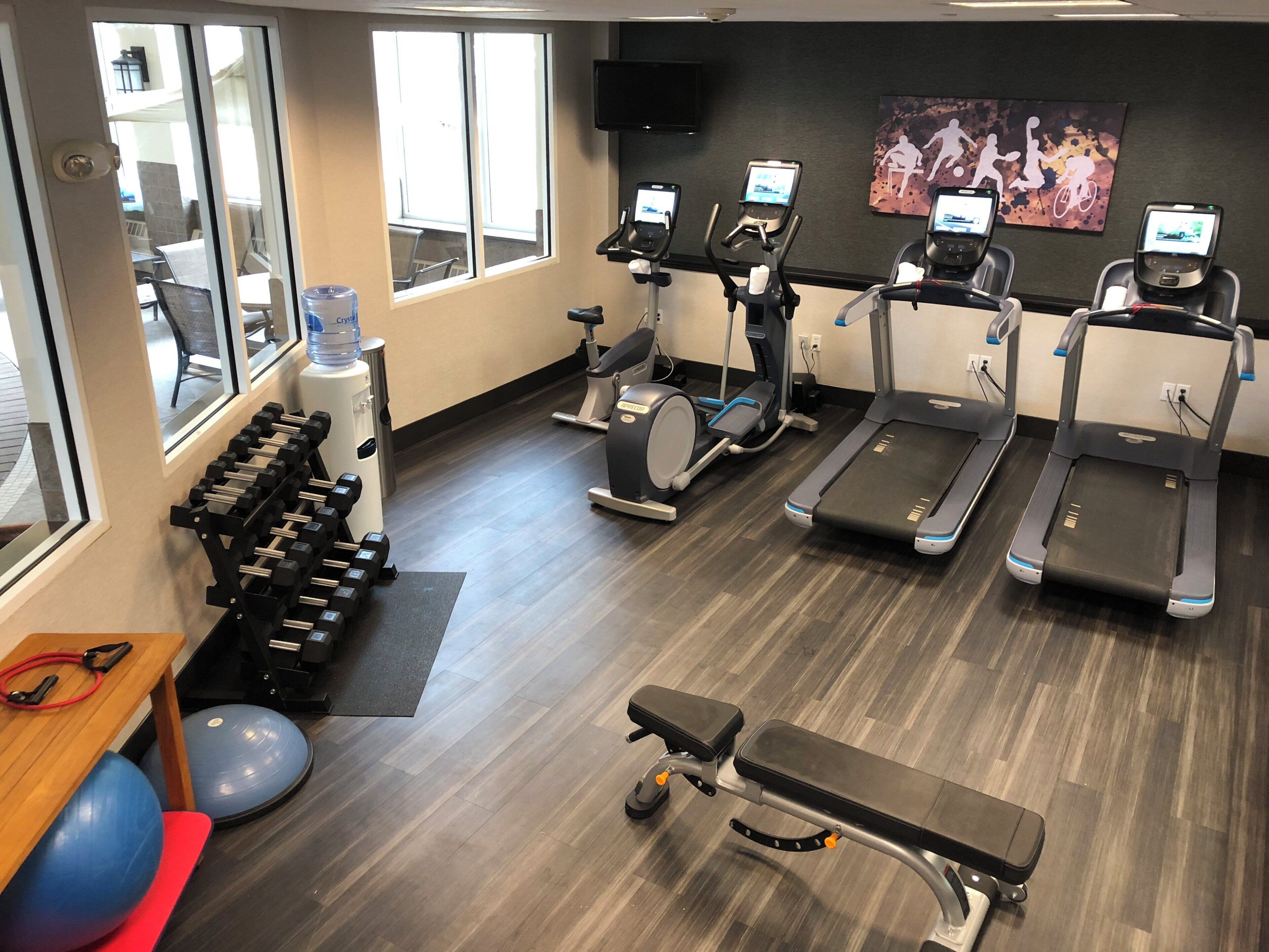 A gym with treadmills, elliptical machines, dumbbells, and exercise balls.