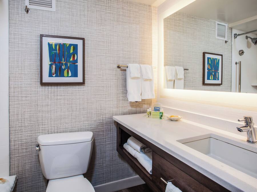 A modern bathroom with a toilet, sink, and shower. There are towels and toiletries on the sink counter.