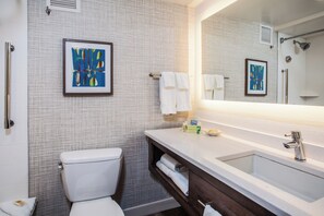 A modern bathroom with a toilet, sink, and shower. There are towels and toiletries on the sink counter.