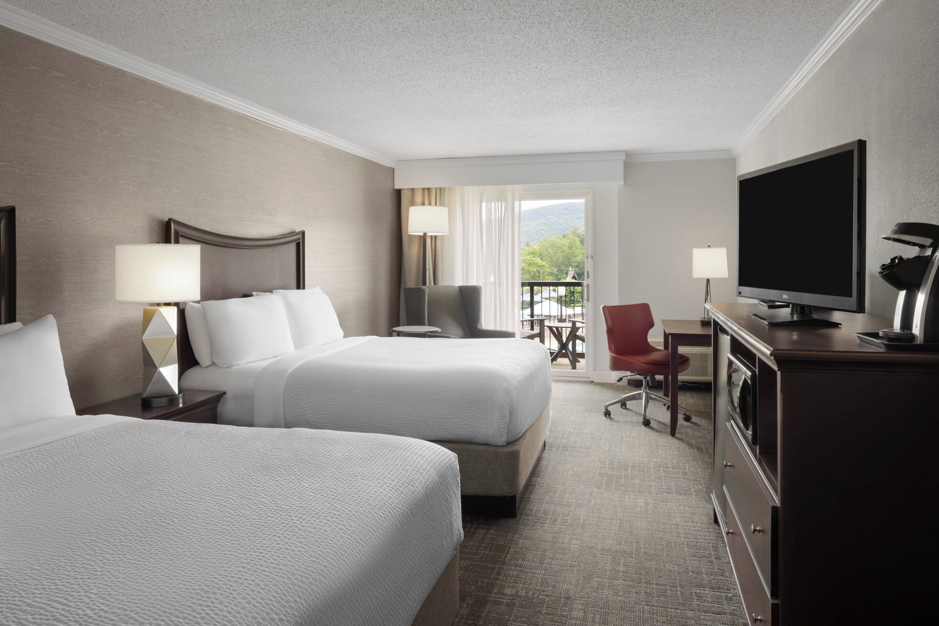 A hotel room with two beds, a TV, a desk, and a chair.