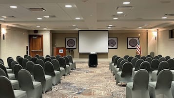 Une salle de conférence avec des rangées de chaises, un pupitre, un écran de projection et un drapeau américain.