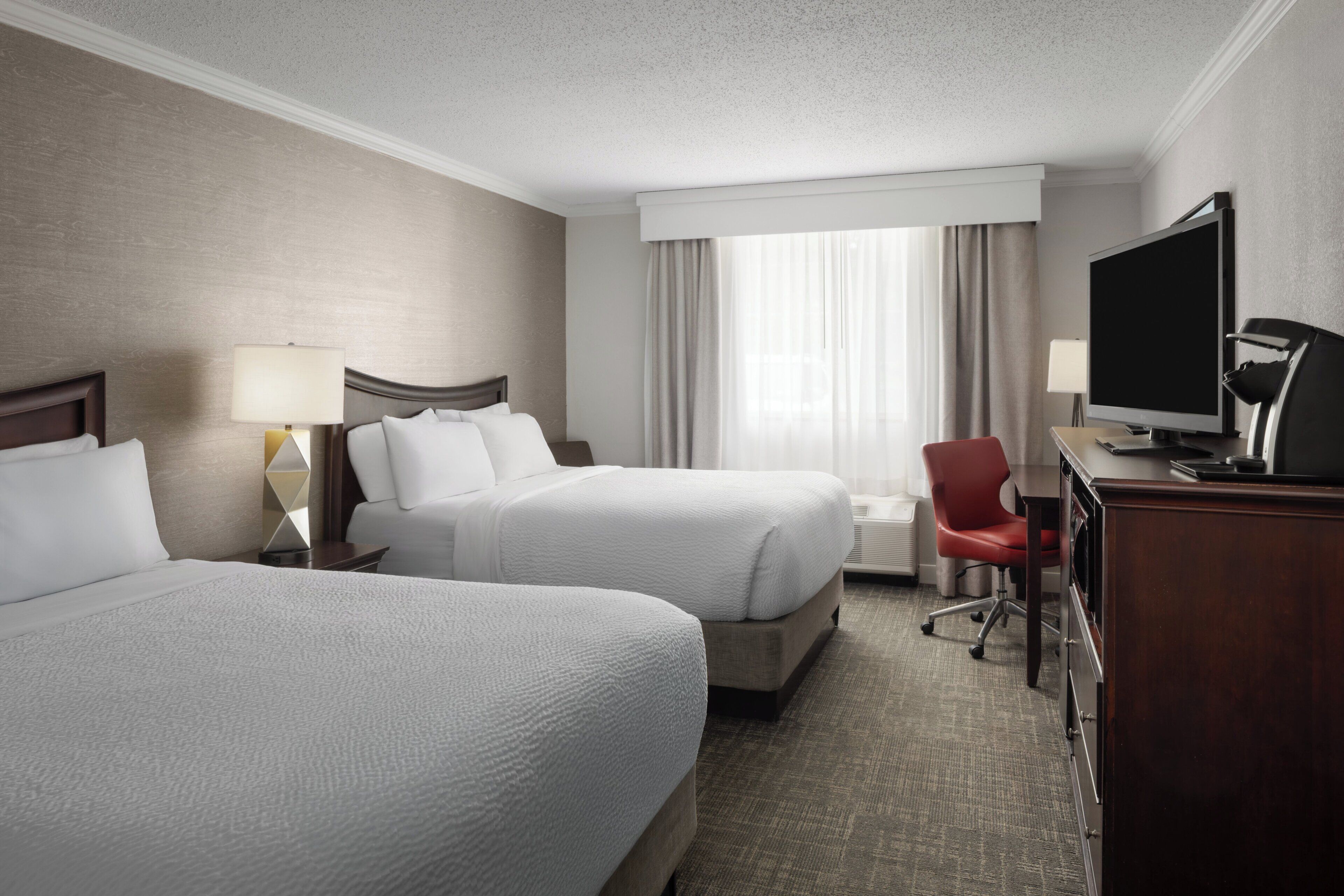 Ein Hotelzimmer mit zwei Betten, einem Schreibtisch mit Computer, einem Fernseher und einem Sessel.