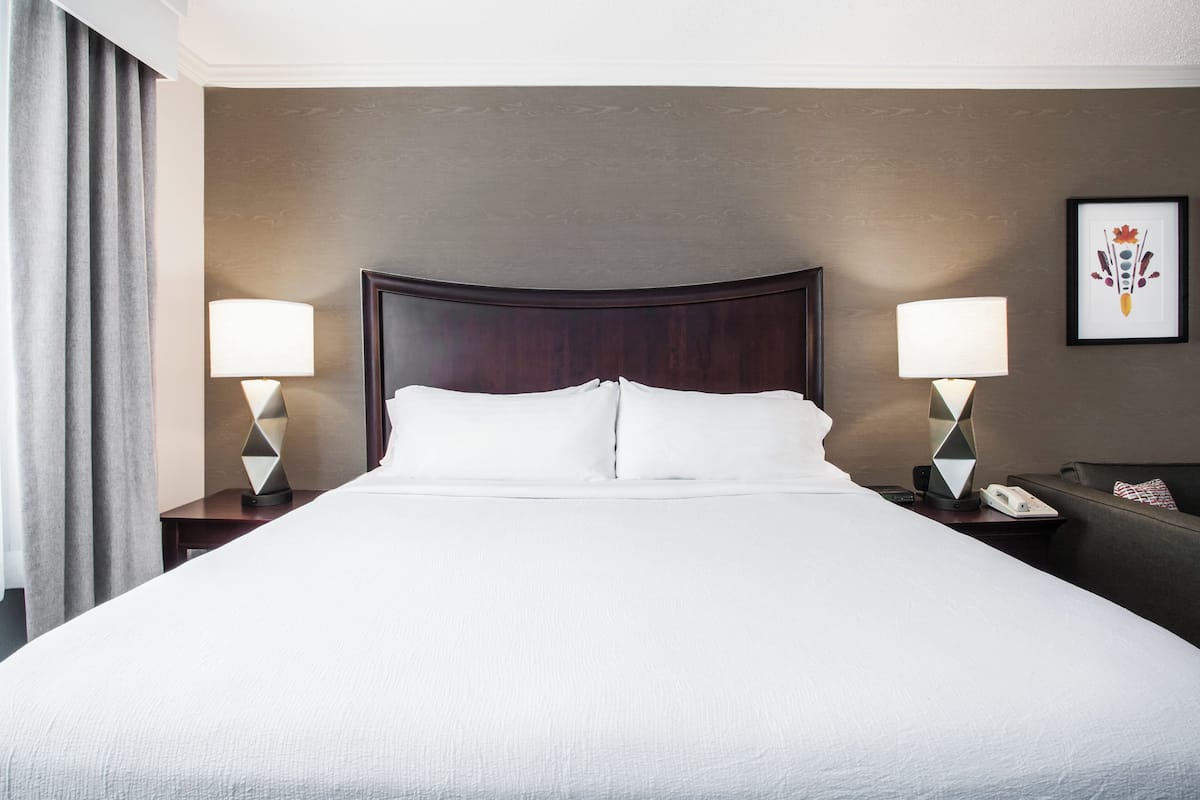 A hotel room with a large bed, two bedside lamps, a nightstand with a phone, and a framed picture on the wall.