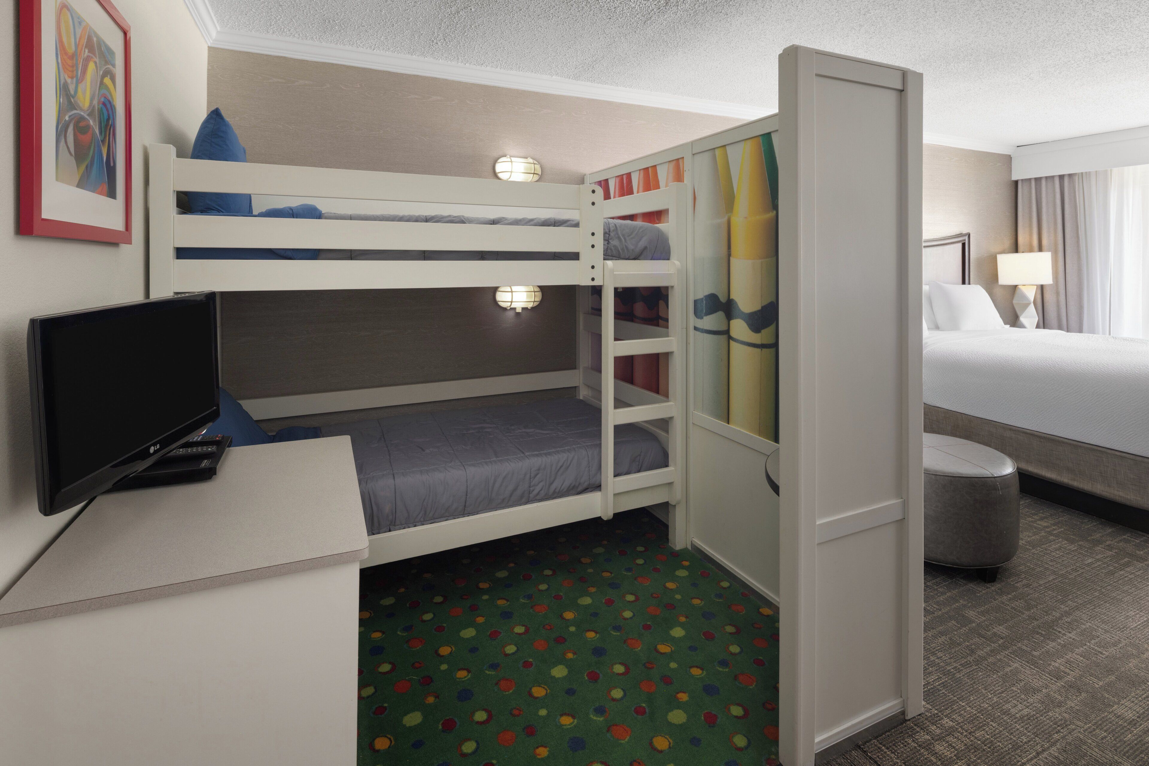 A hotel room with a bunk bed, a desk with a television, and a small trash bin.