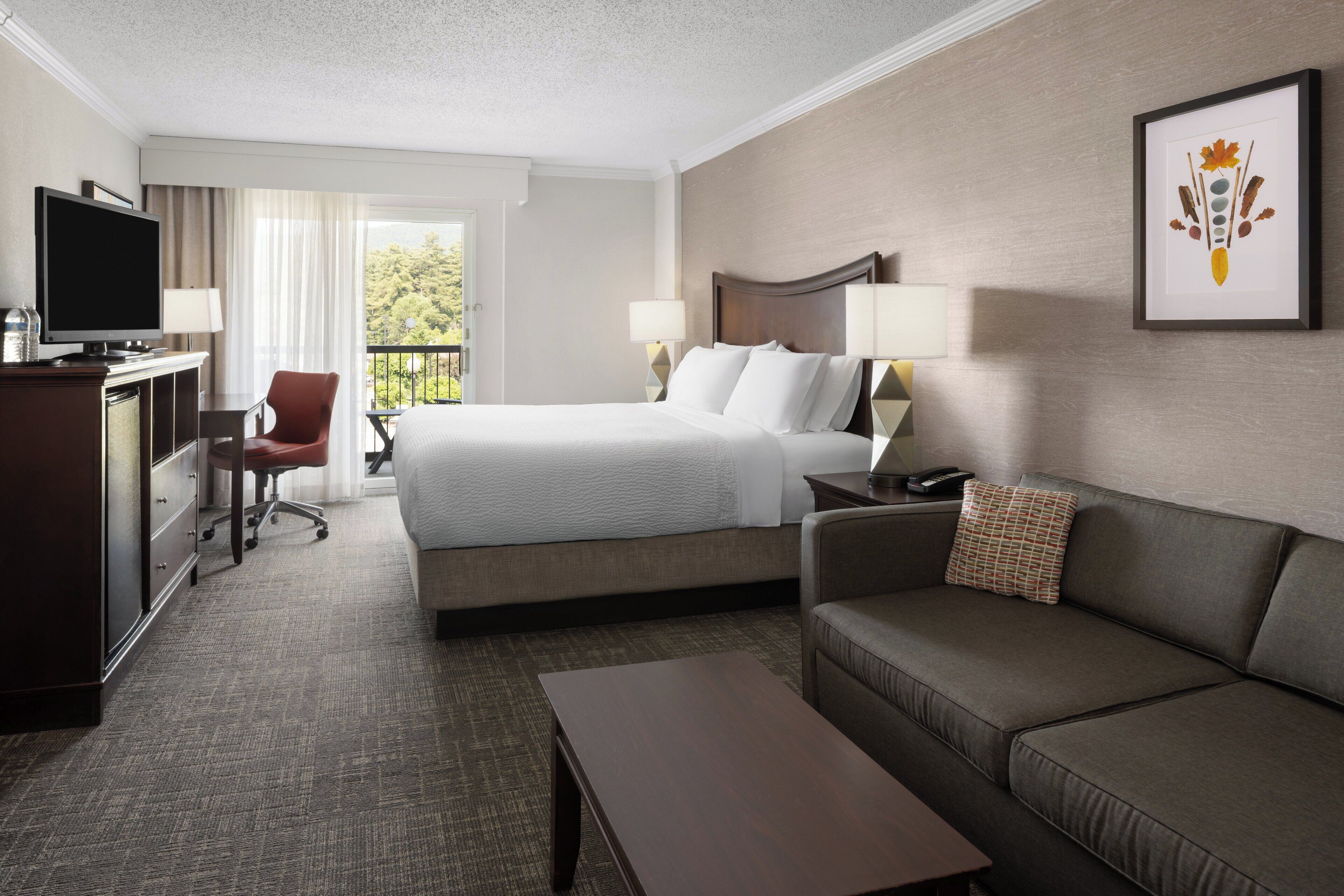 A hotel room with a bed, a desk with a TV, a sofa, and a coffee table.