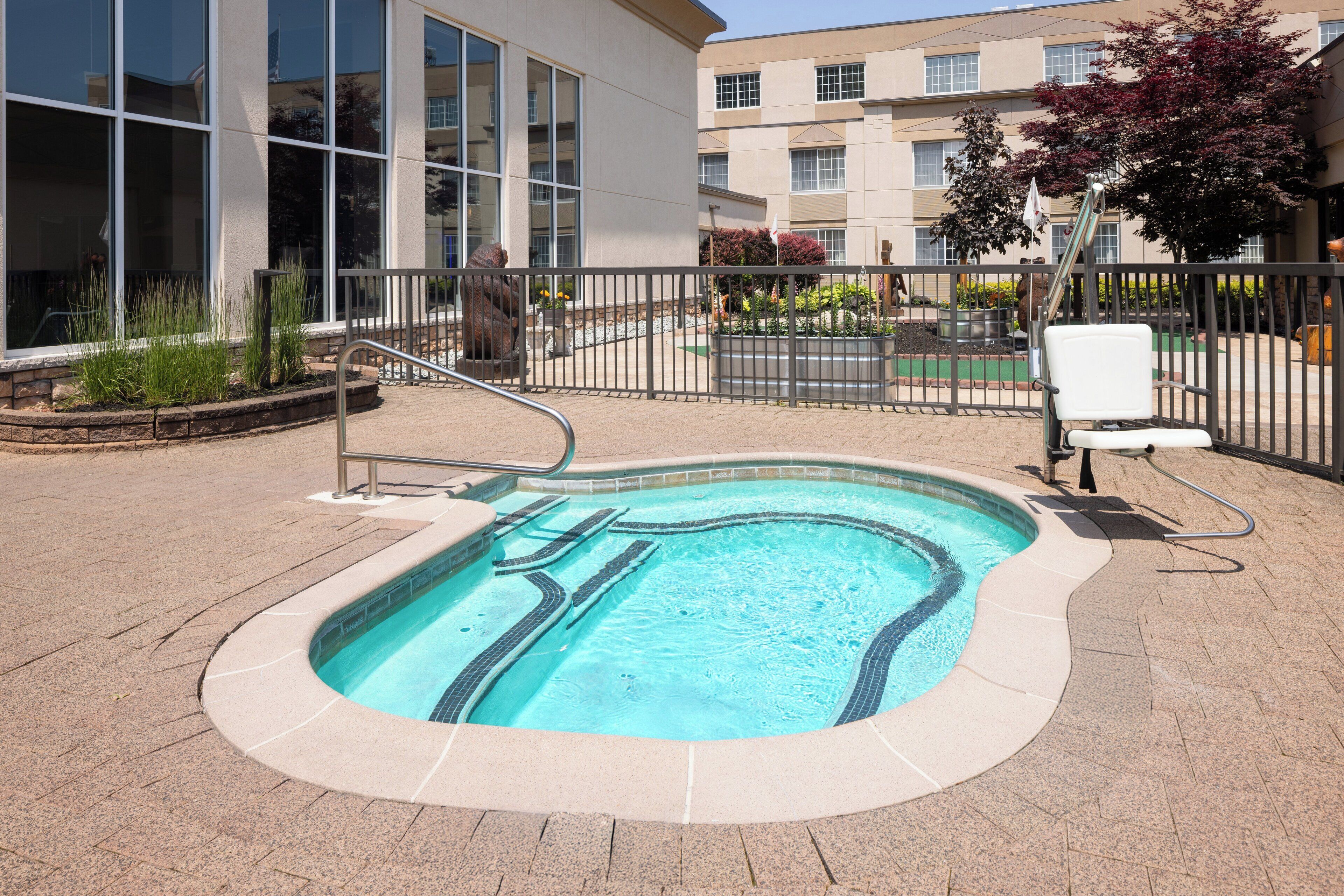A swimming pool with a tiled deck, surrounded by a metal fence, and a chair.