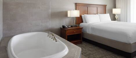 A hotel room with a large bathtub, a wooden headboard, a bed with white linens, and two bedside lamps.