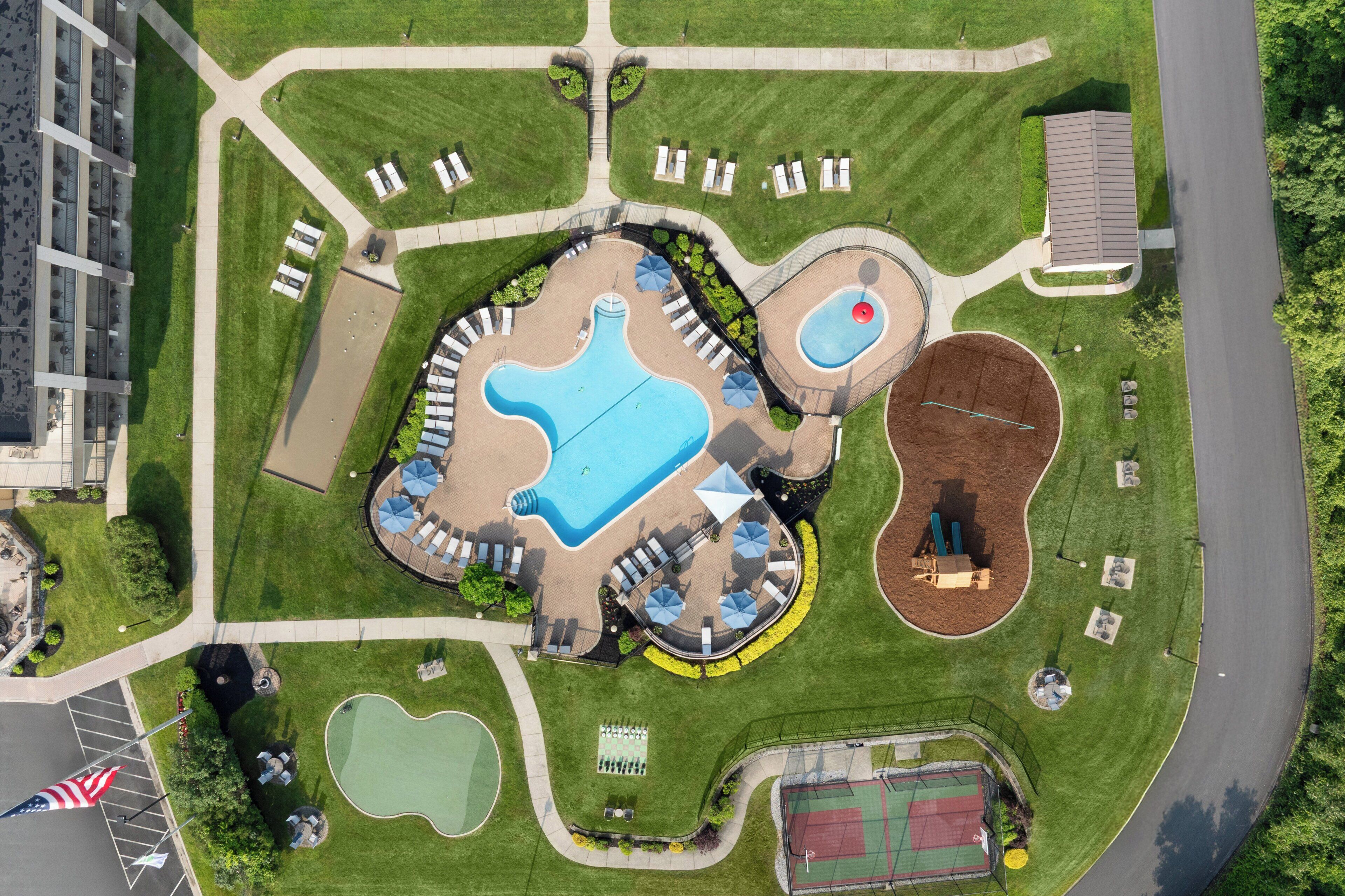 Vue aérienne d’un parc comprenant une grande piscine, un court de tennis et un terrain de basketball.