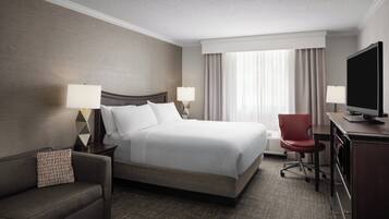 A hotel room with a large bed, two bedside lamps, a TV, a desk, and a chair.
