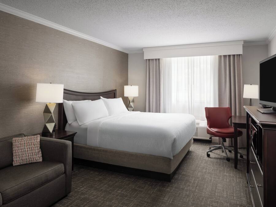 A hotel room with a large bed, two bedside lamps, a TV, a desk, and a chair.