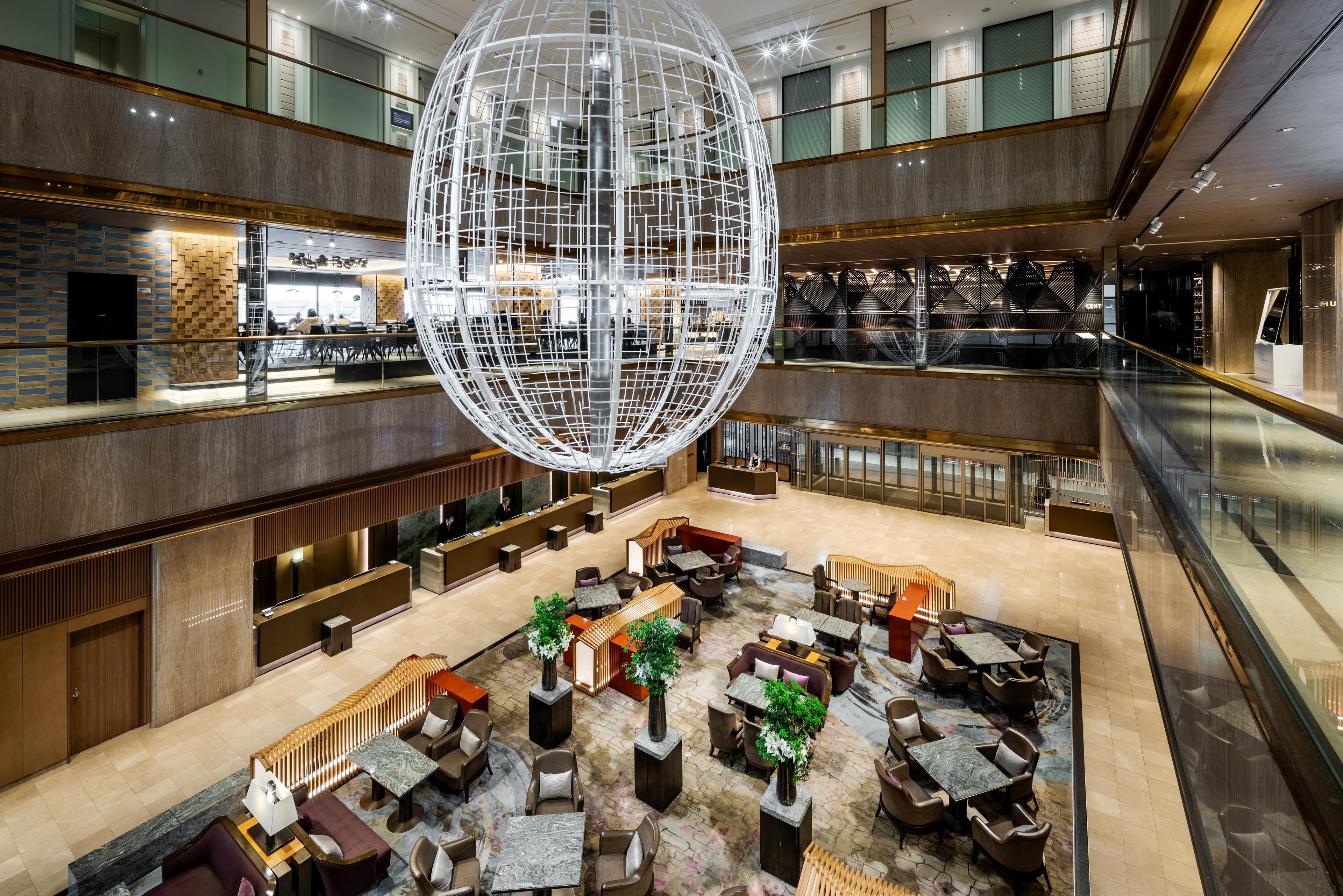 A spacious lobby with a large spherical light fixture, multiple seating areas, and a high ceiling.