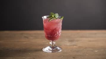 A tall glass with a floral pattern filled with a red beverage, garnished with a mint leaf, placed on a wooden surface.