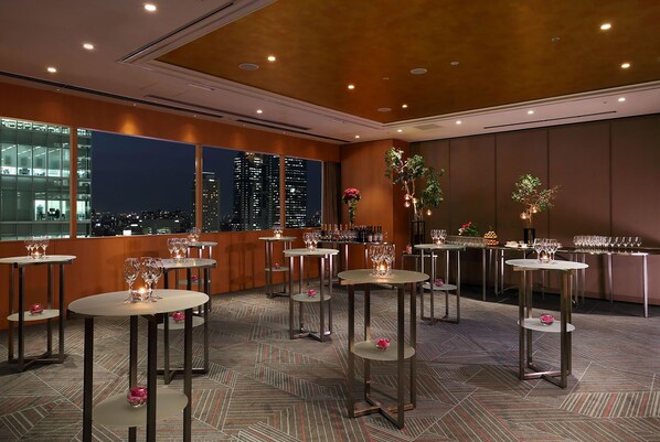 A hotel room with multiple tables set for dining, a city view, and a large window.