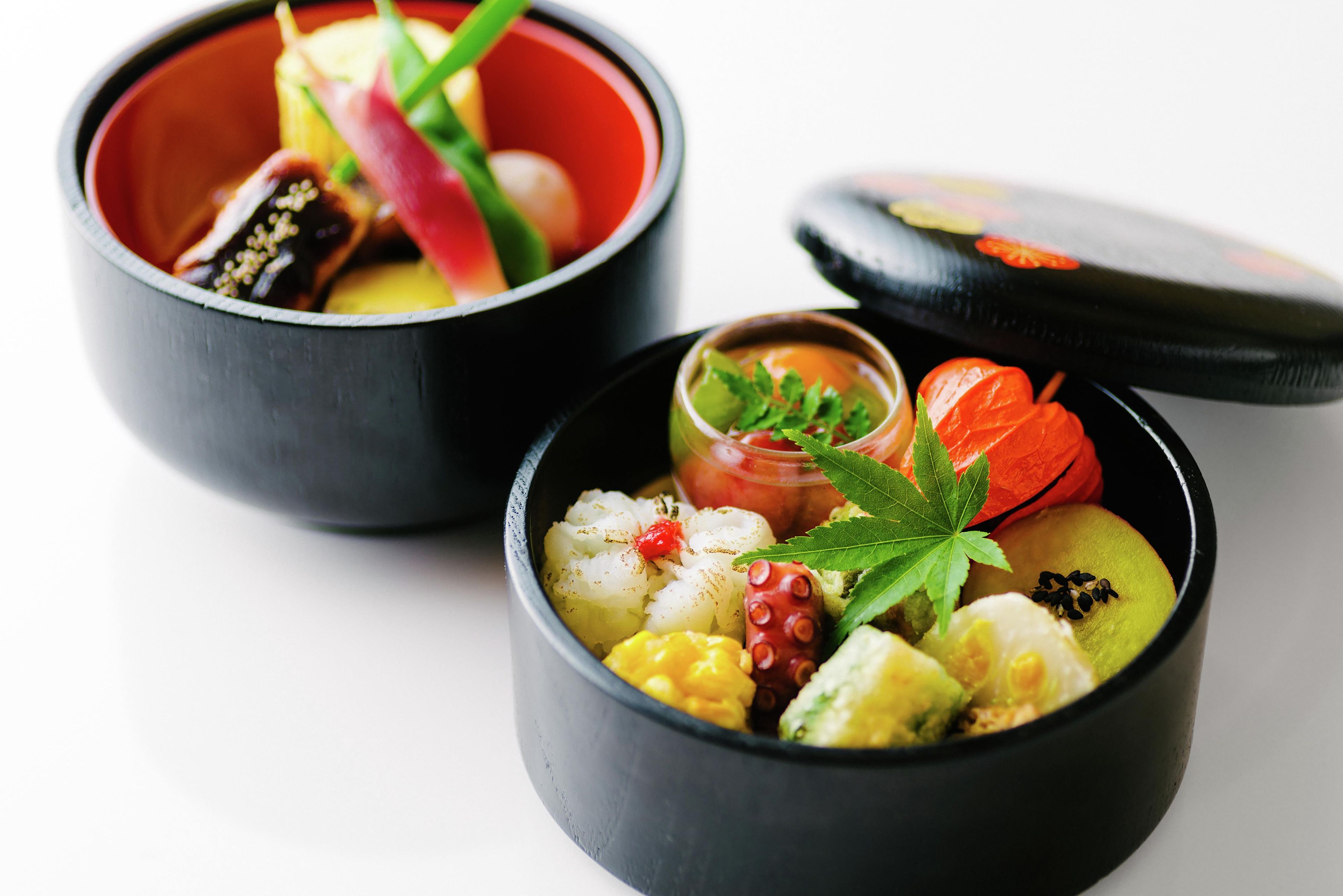 Two black bowls with food and garnishes on a white surface.