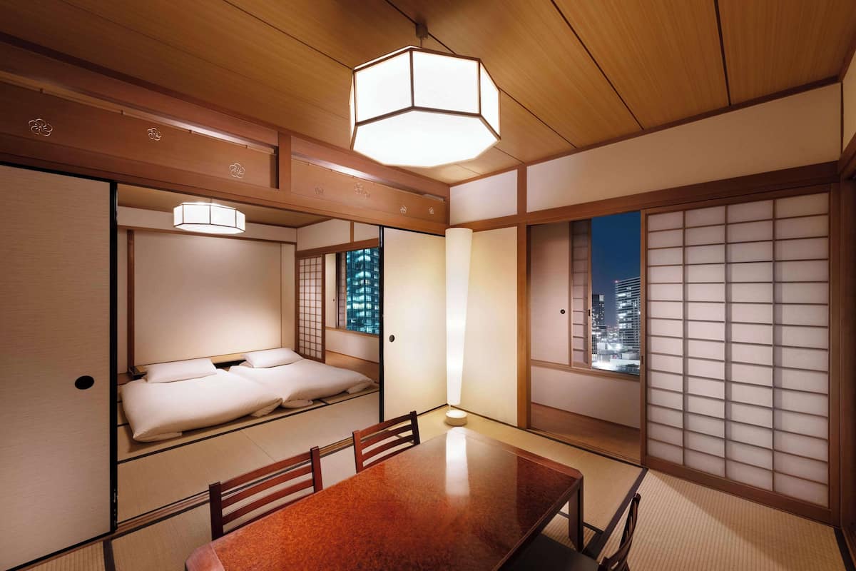 A traditional Japanese room with tatami flooring, a low table, and a bed with white bedding.