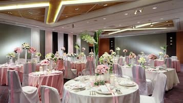 Un salón de banquetes con mesas redondas, manteles rosa y blancos y centros de mesa florales.