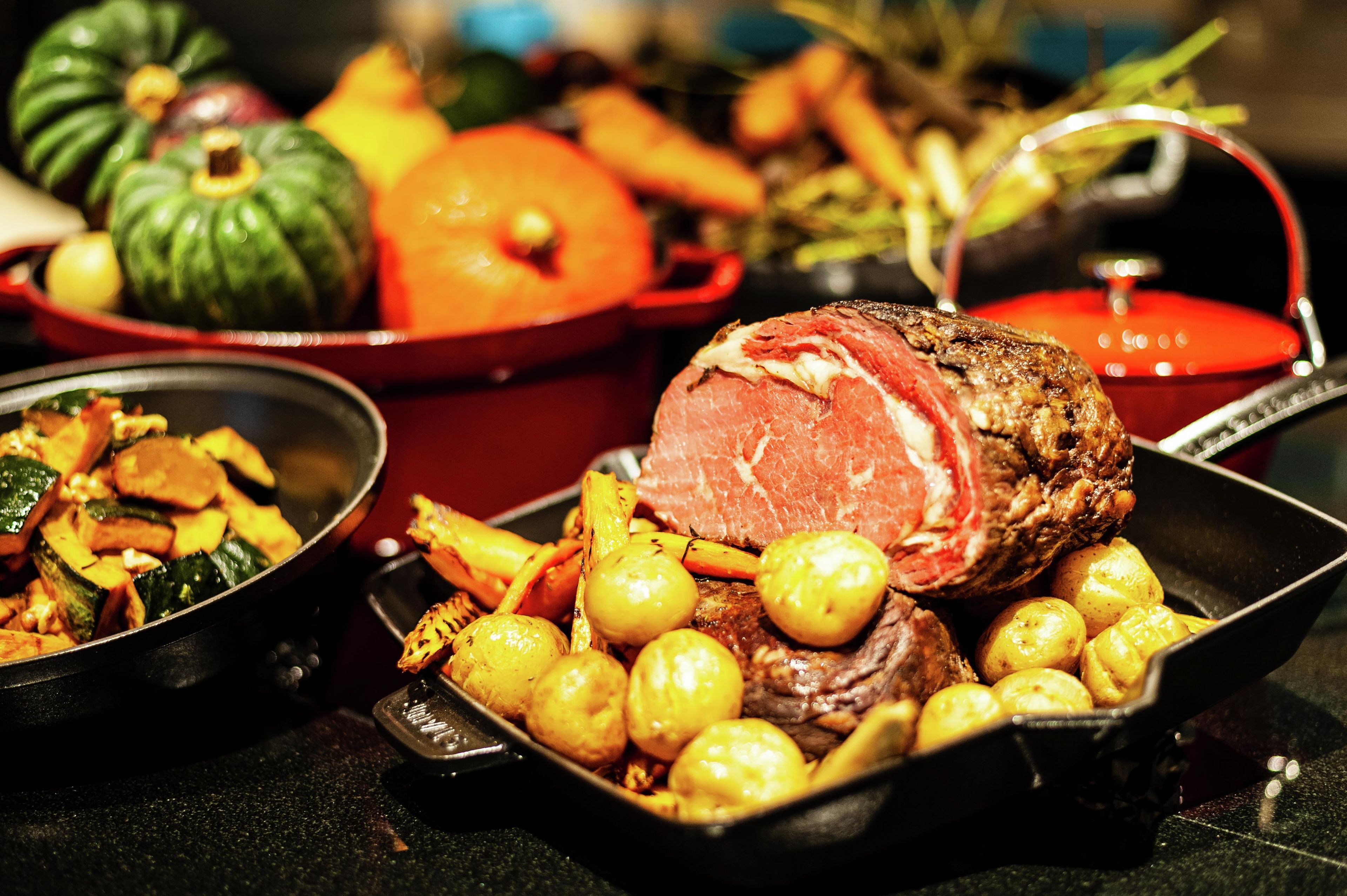 A variety of dishes including roasted vegetables and a large piece of meat, likely beef, served on a table.