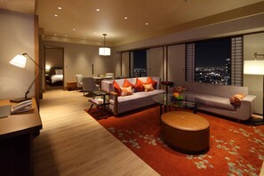A modern hotel room with a sofa, armchairs, a coffee table, and a view of the city at night. - Hilton Osaka (Osaka)