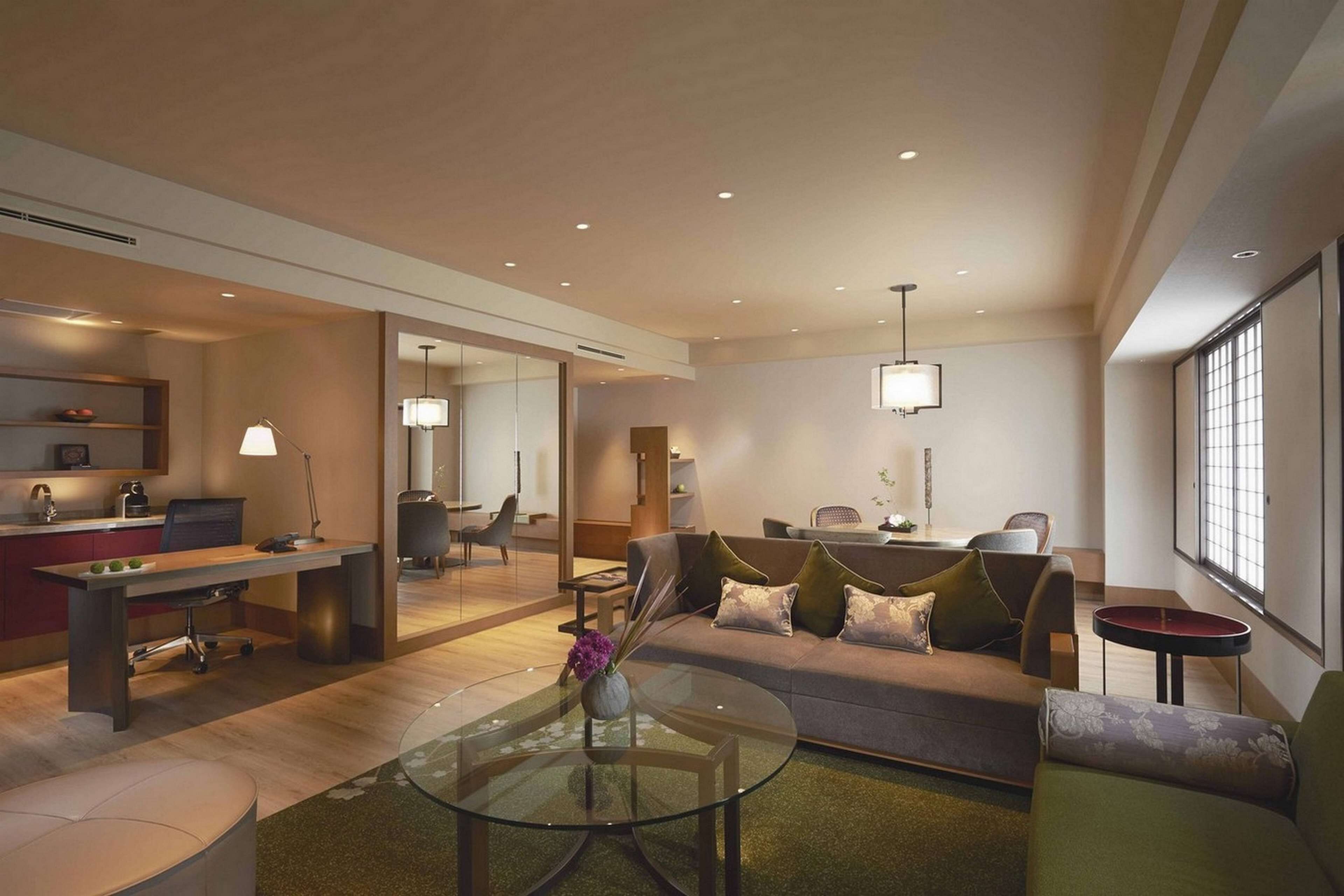 A modern living room with a glass coffee table, a sofa, and a dining area with a table and chairs.