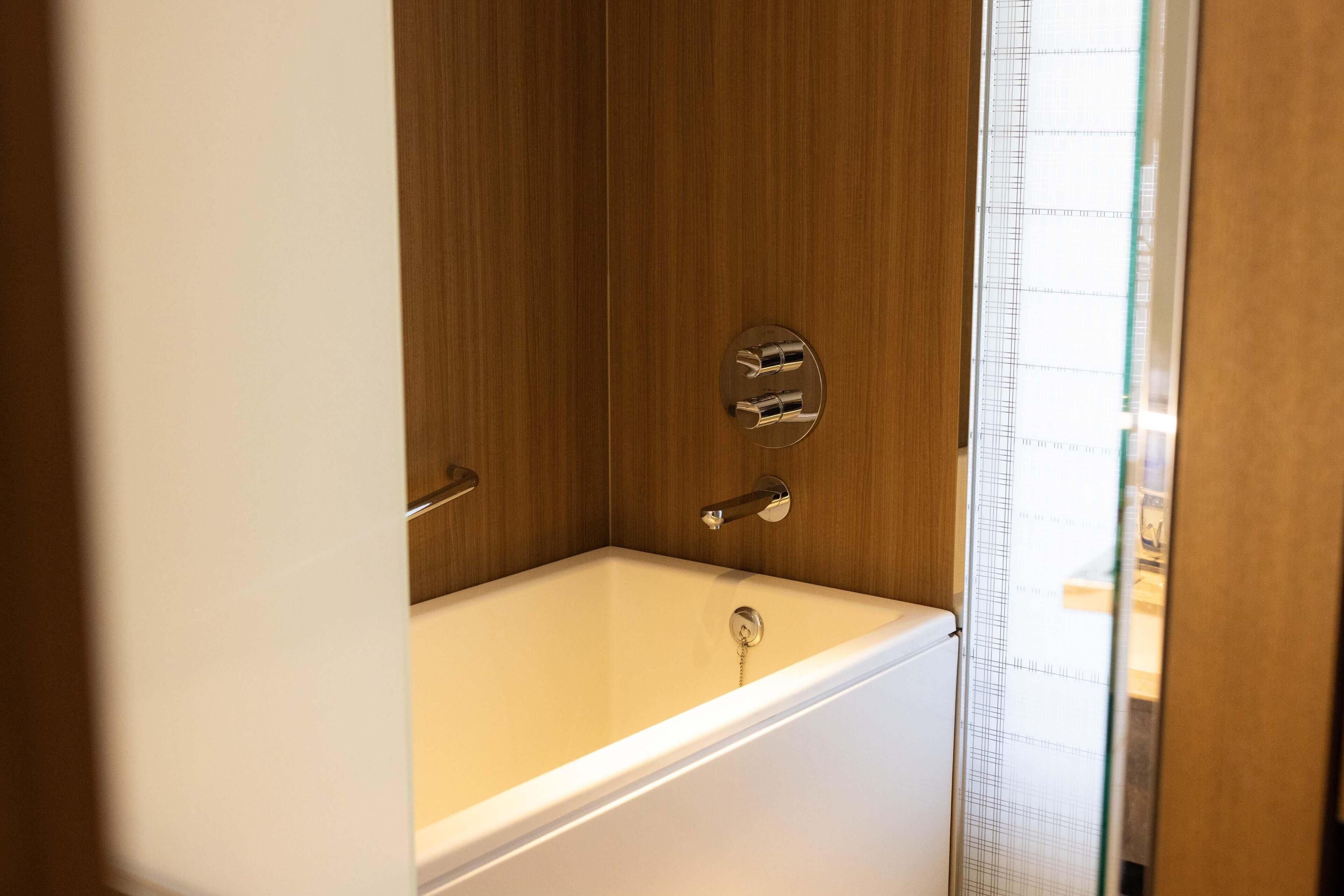 A bathroom with a wooden wall, a bathtub, and a shower area.