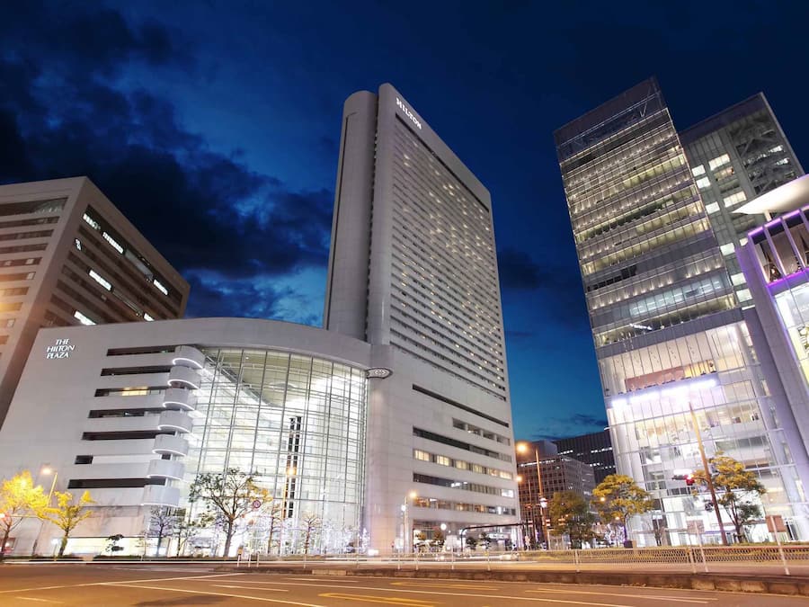 Un hotel moderno con fachada curva y grandes ventanales, rodeado de otros edificios altos.