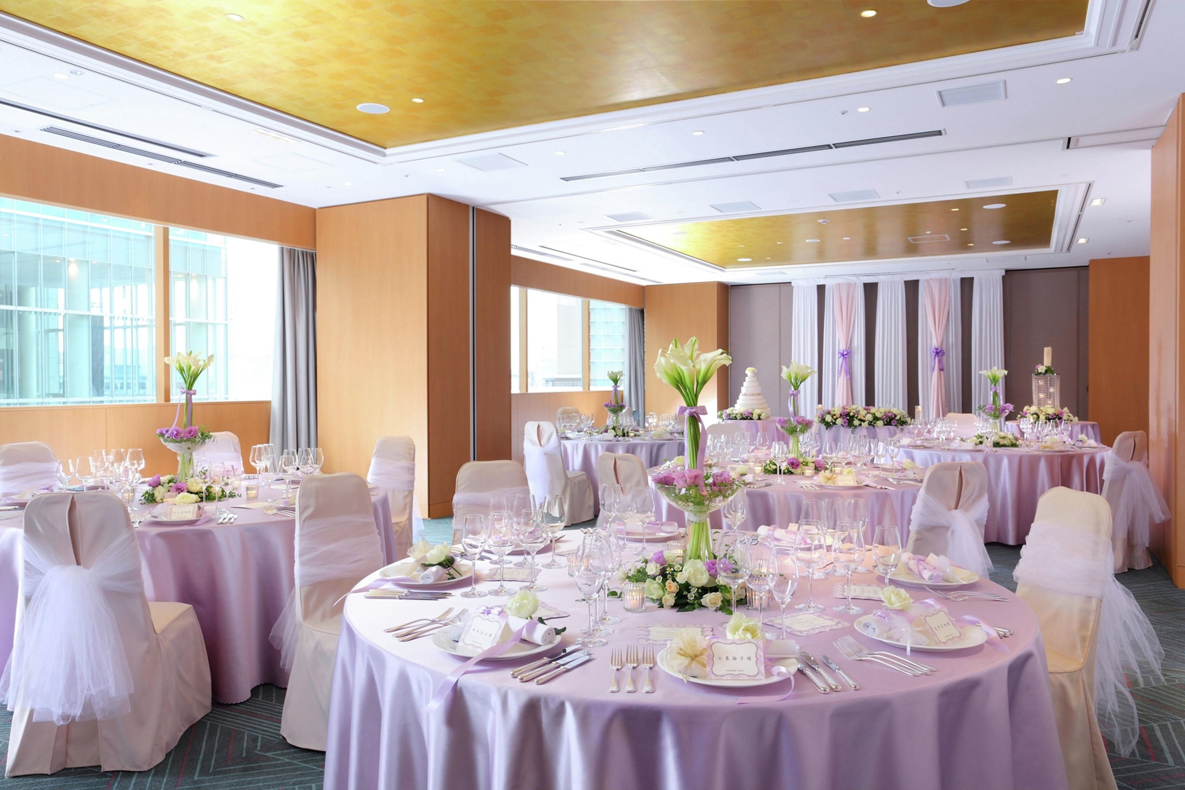 A banquet hall with round tables, white chairs, and floral centerpieces.