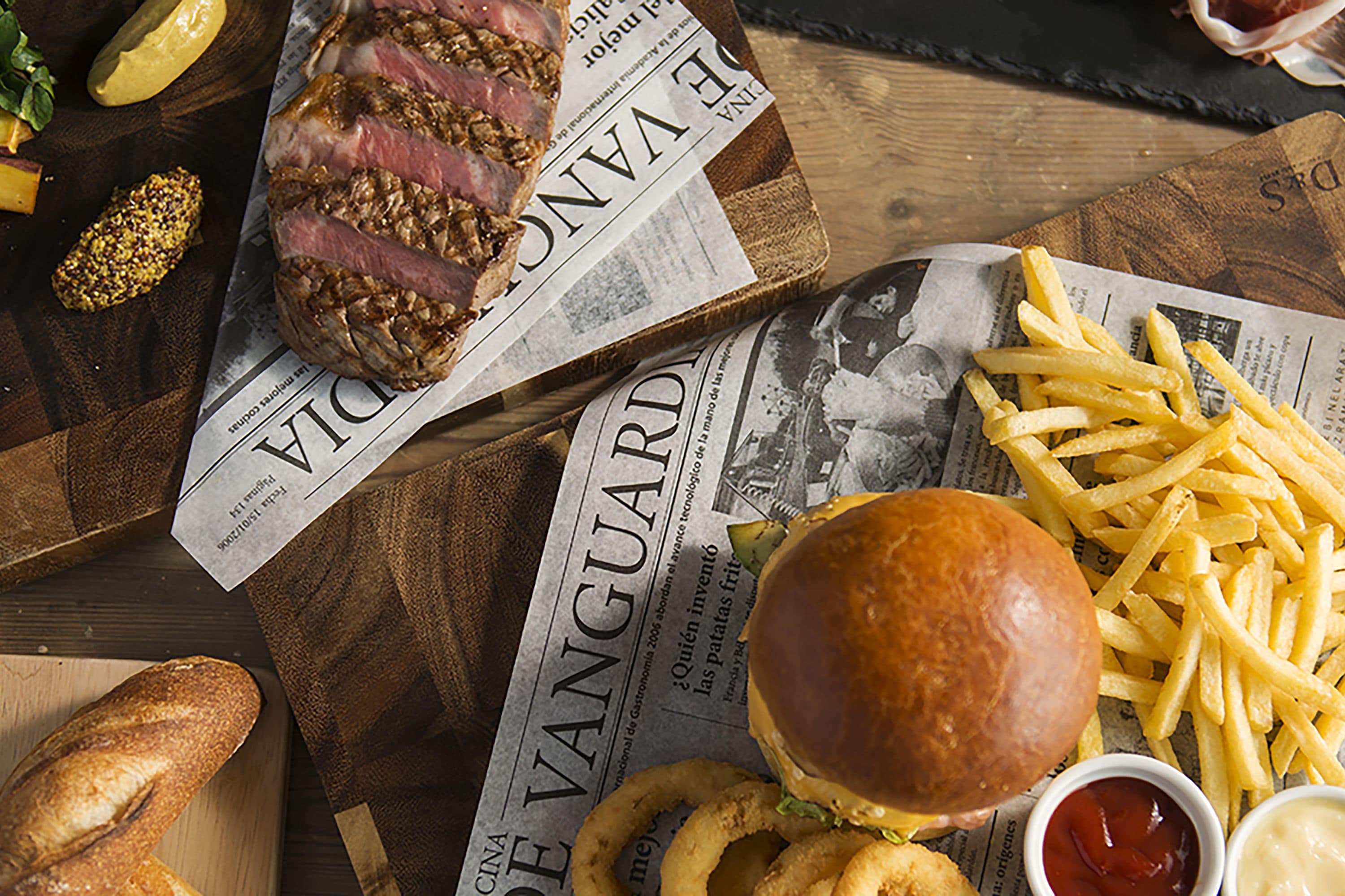 A meal with a sandwich, fries, and a steak on a wooden board.