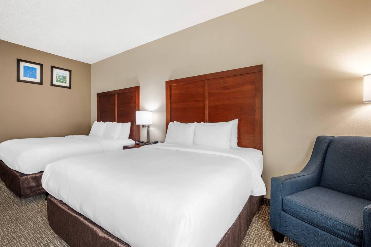 A hotel room with two beds, a nightstand, a lamp, and a blue armchair.