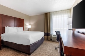 A hotel room with a large bed, a desk, a chair, a lamp, and a television.
