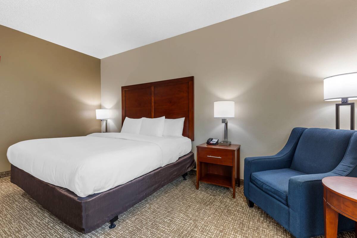 A hotel room with a large bed, bedside tables, a chair, and a lamp.
