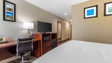 Une chambre d’hôtel équipée d’un lit, d’un bureau, d’une chaise, d’une télévision, d’un four à micro-ondes et de tableaux encadrés aux murs.