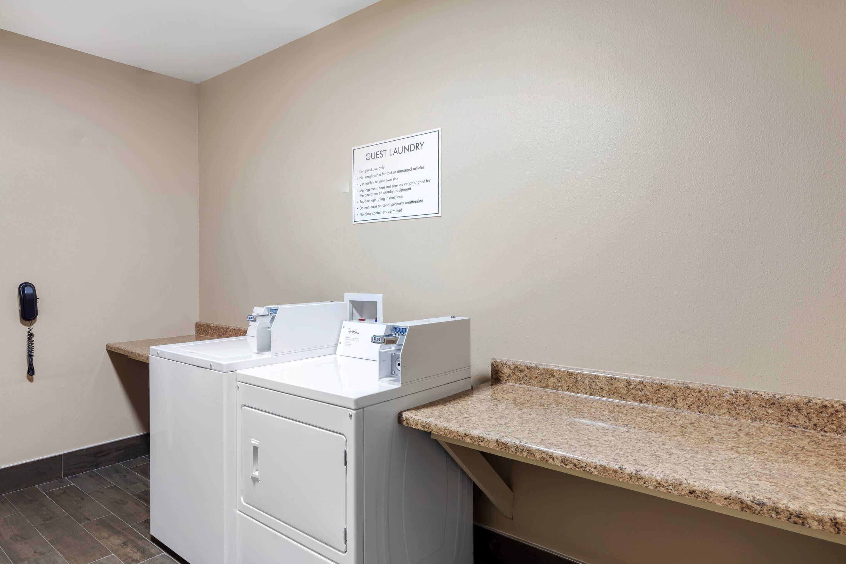 A guest laundry area with a washing machine, a dryer, a phone, and a sign detailing laundry rules.