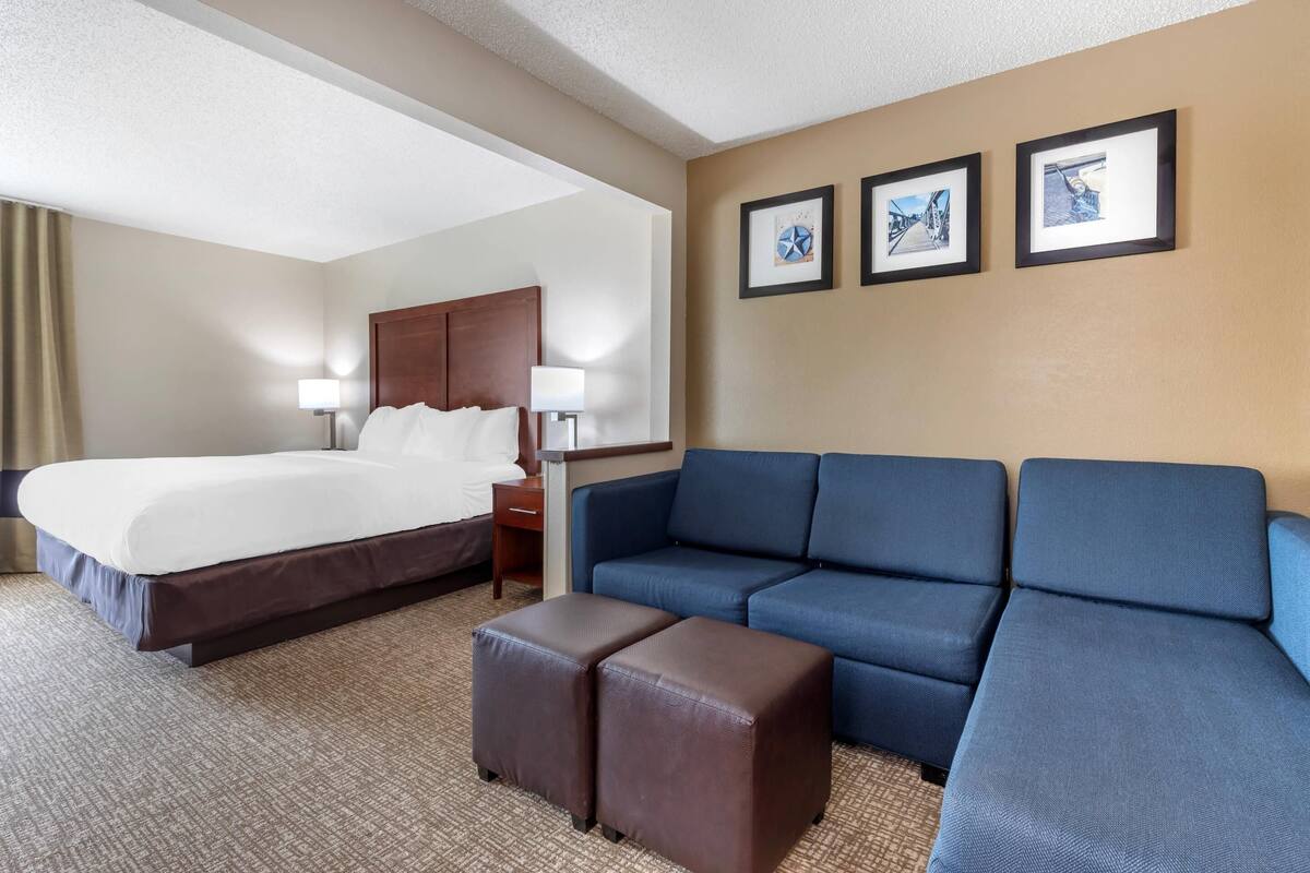A hotel room with a bed, a blue sofa, an ottoman, and framed pictures on the wall.