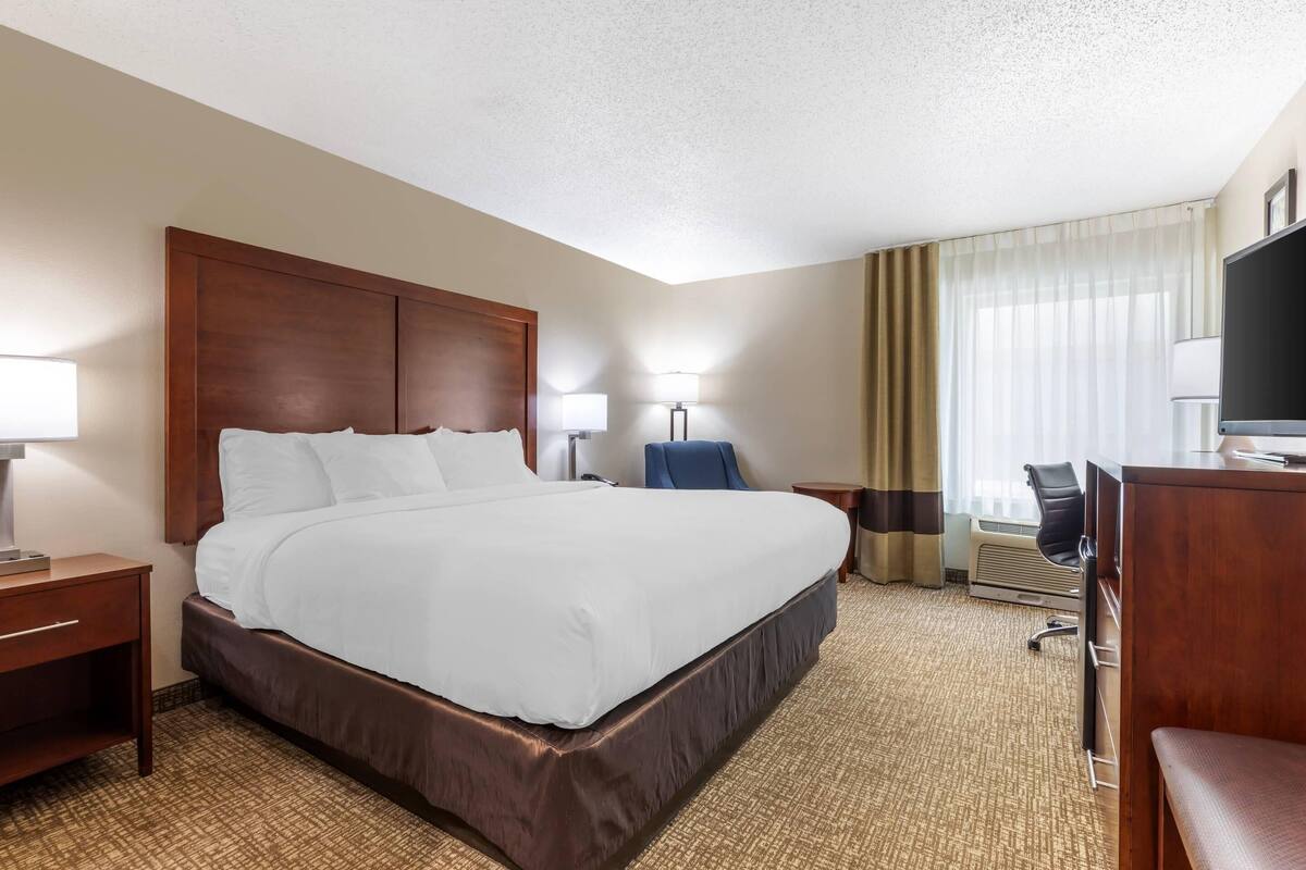A hotel room with a large bed, a desk, a chair, a TV, and a window with curtains.