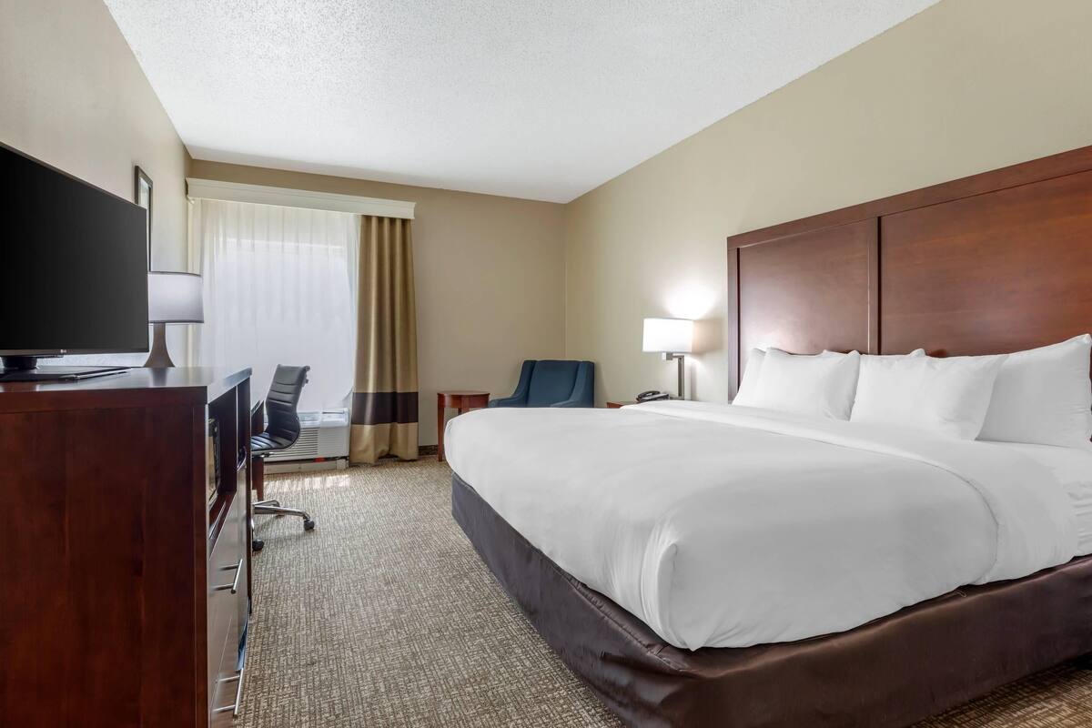 A hotel room with a large bed, a desk with a TV, a chair, a lamp, and a window with curtains.