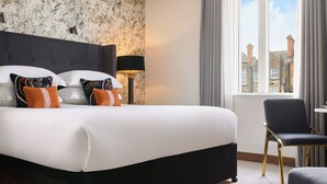 A modern hotel room with a large bed, a desk, and a view of the city.
